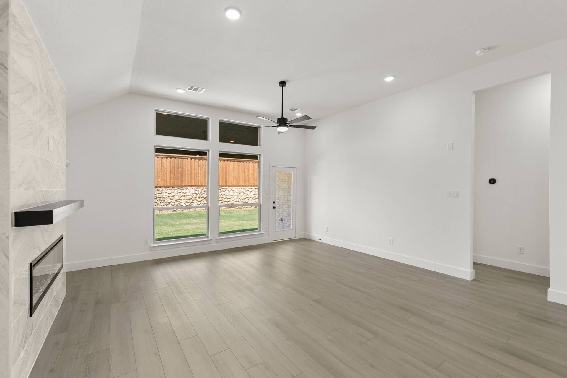 Modern living room with large windows, ceiling fan, and hardwood floors.