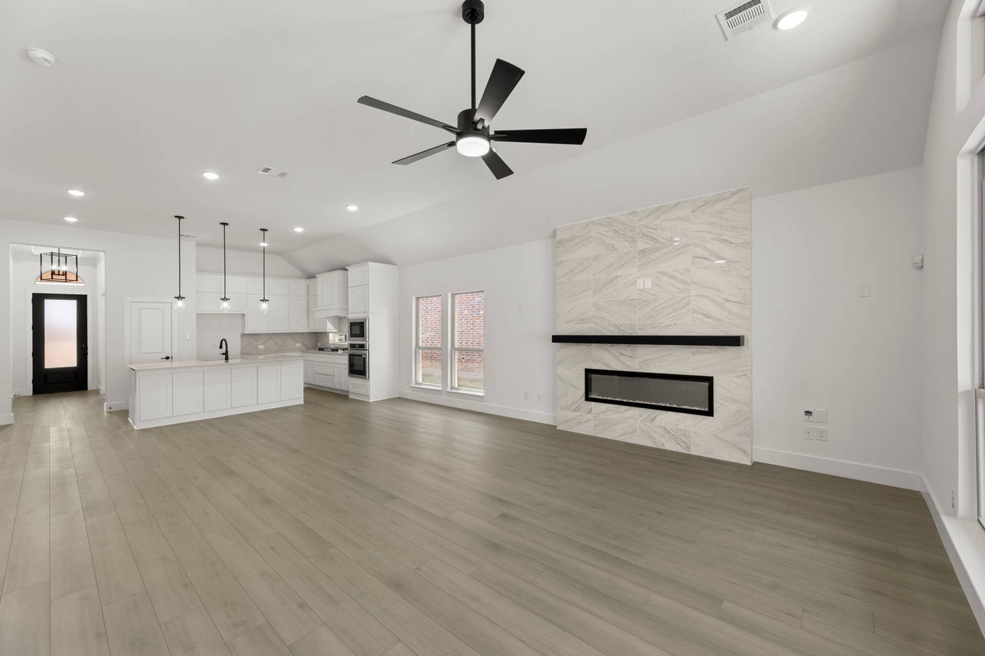 Spacious modern kitchen and living area with marble fireplace and ceiling fan.