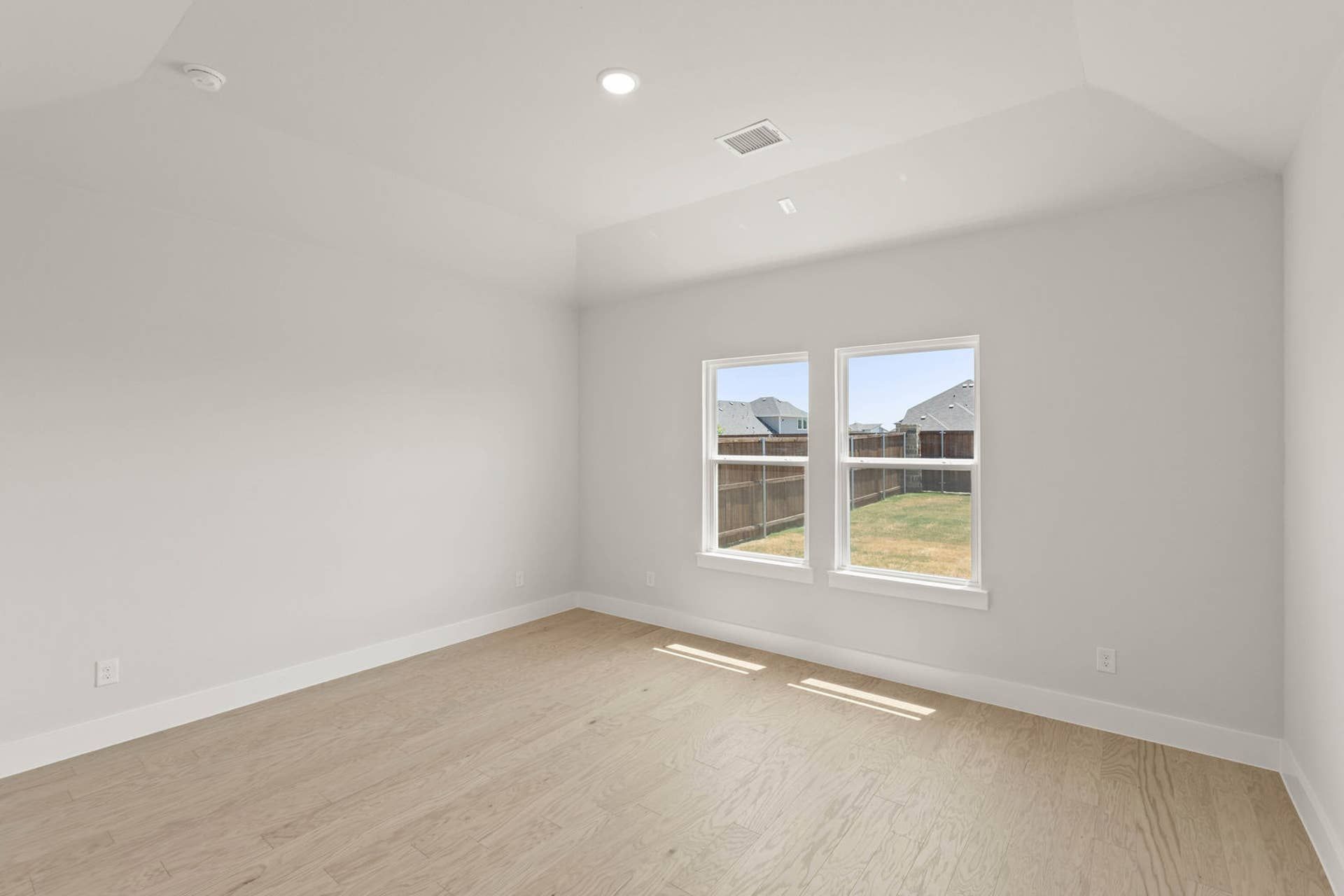 Spacious primary suite with large windows and hardwood flooring.
