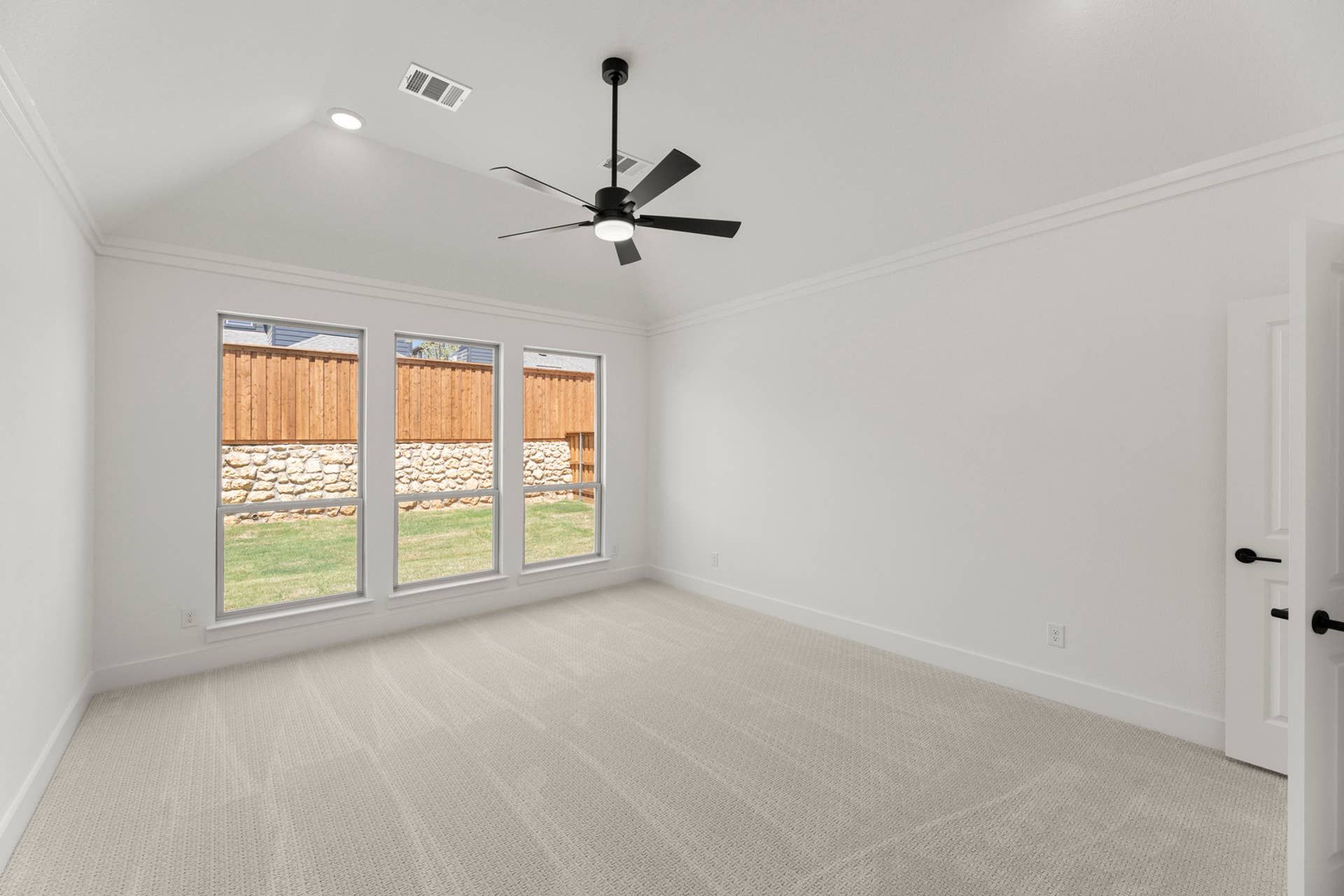 Spacious room with vaulted ceiling, ceiling fan, and large windows overlooking backyard.
