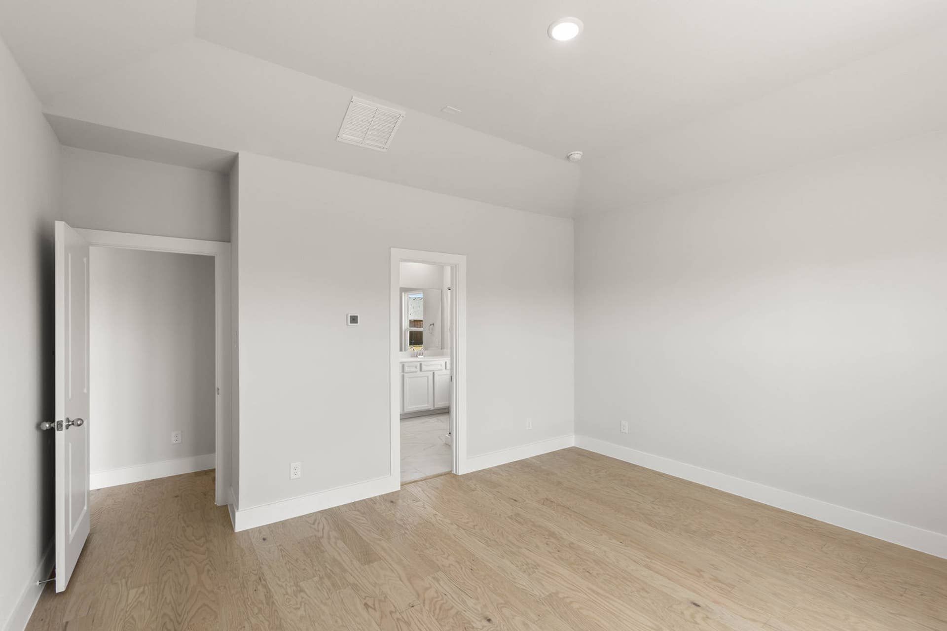 Spacious primary suite with hardwood floors and neutral walls.