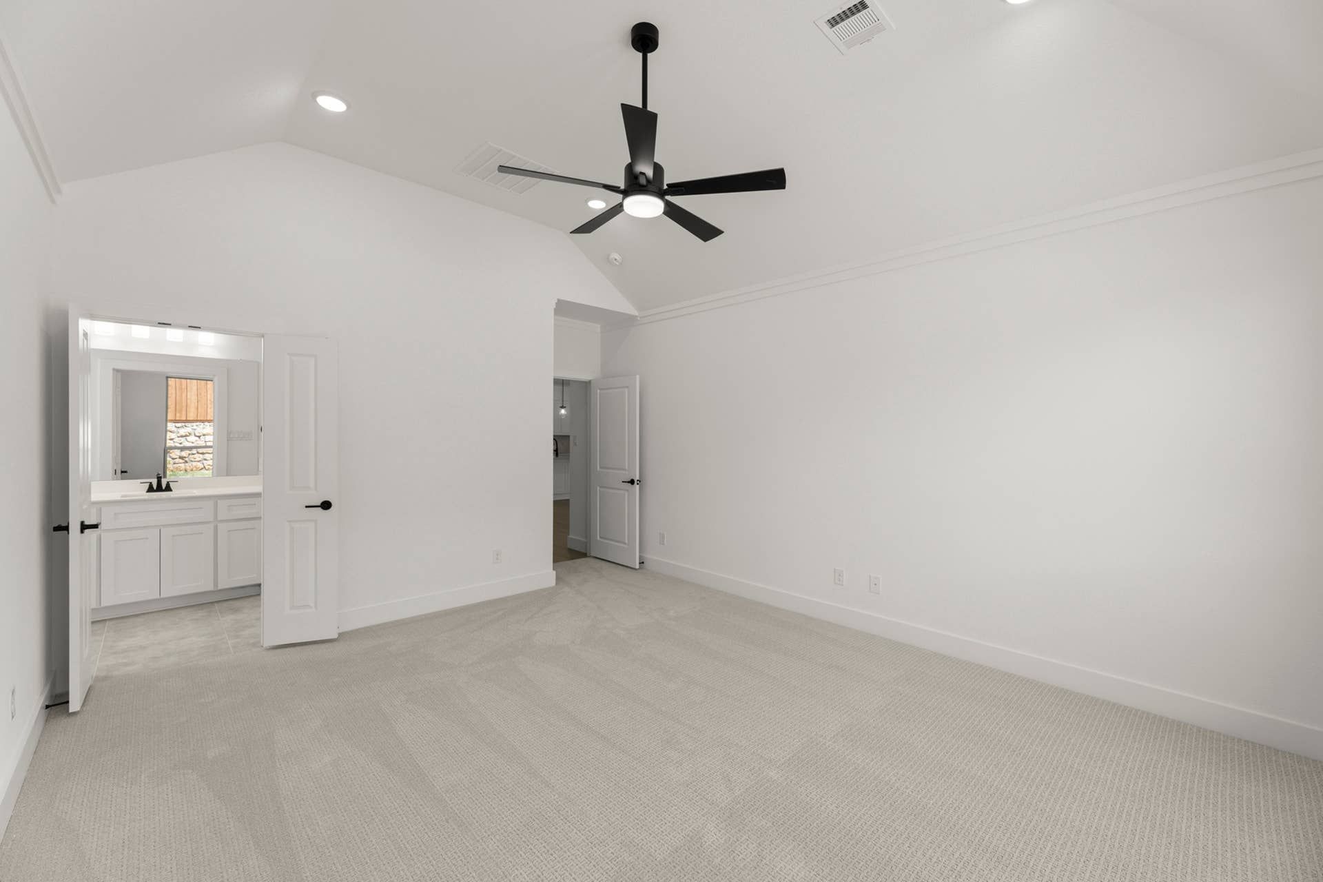 Spacious, bright room with ceiling fan and carpeted floor, leading to a bathroom.