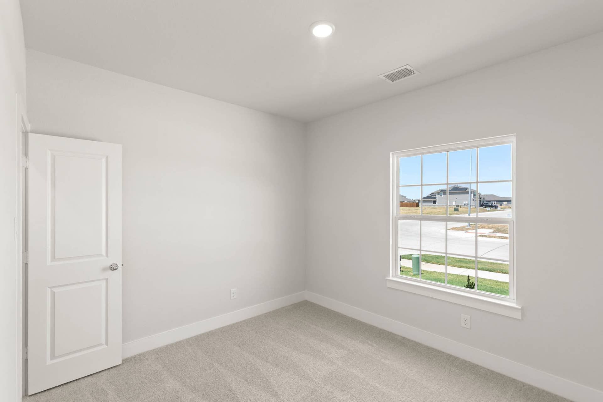 Bright bedroom with white walls, carpeted floor, and large window view.