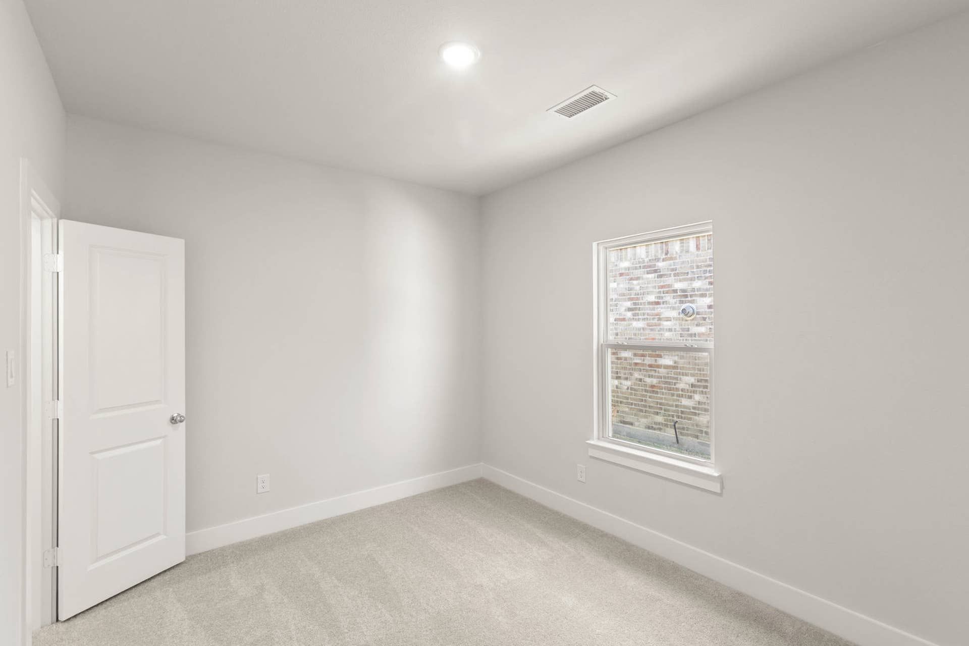 Bright, empty bedroom with neutral walls and carpet, featuring a single window and door.