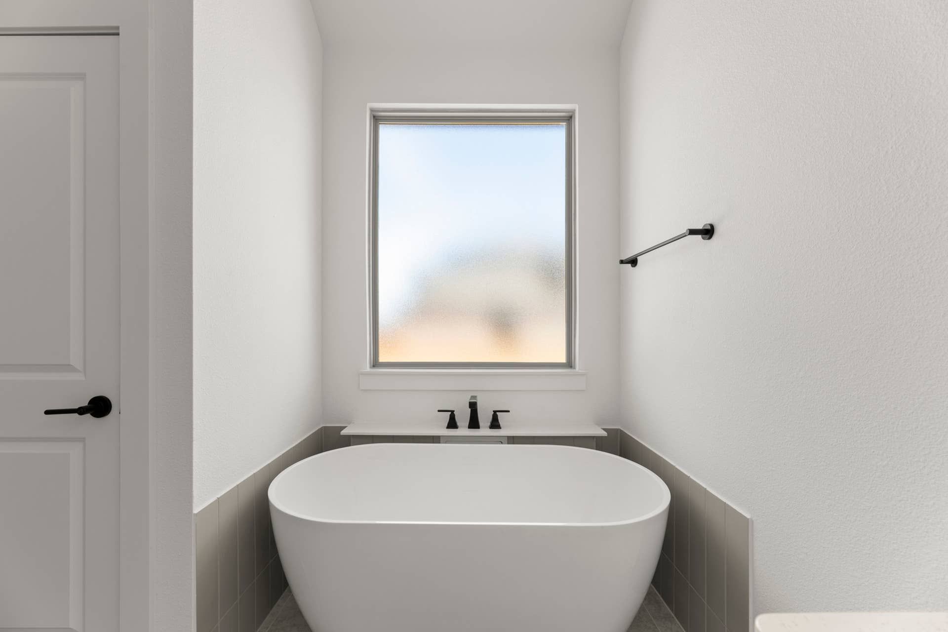 Modern bathroom with freestanding tub and frosted window.