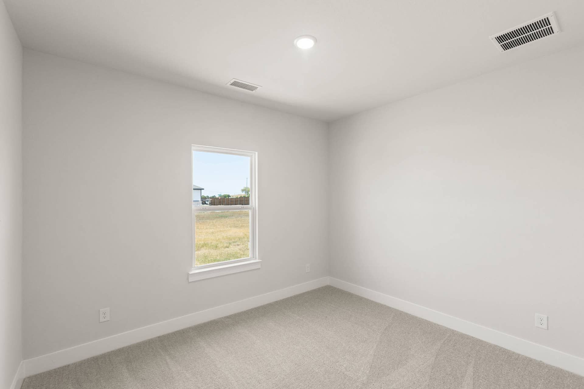 Minimalist bedroom with neutral walls, carpet flooring, and a single window view.