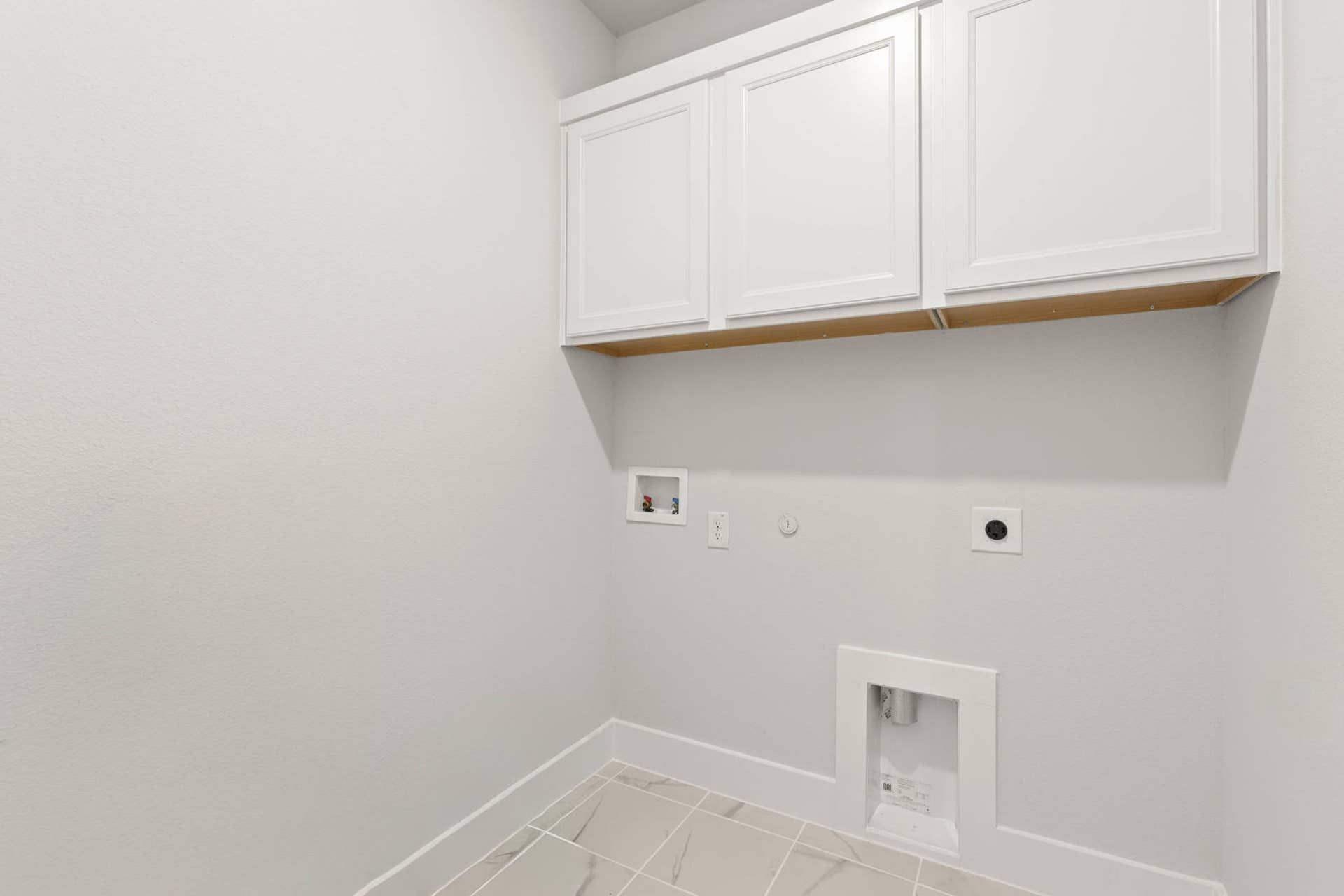Utility room with white cabinets and laundry hookups.