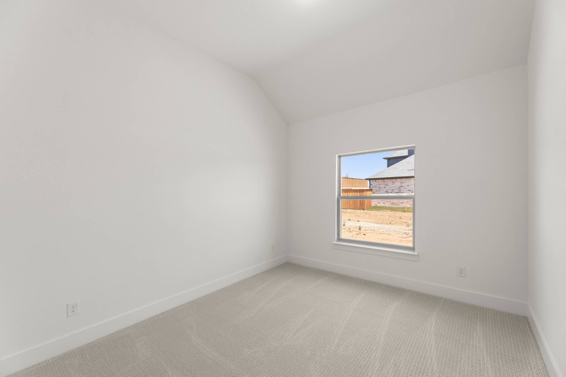 Bright, unfurnished bedroom with carpet and a large window overlooking a yard.