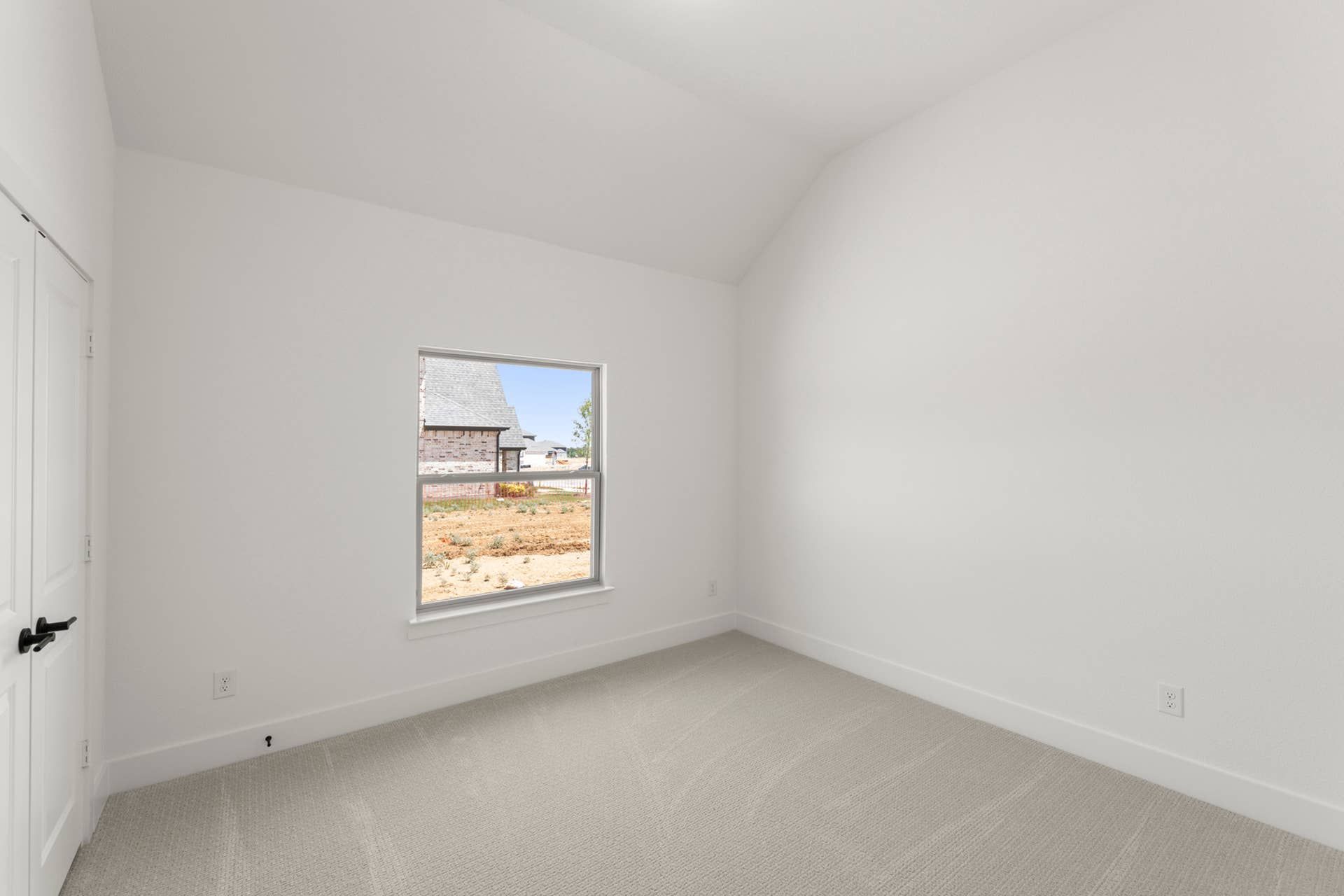 Spacious bedroom with white walls and a window overlooking the yard.