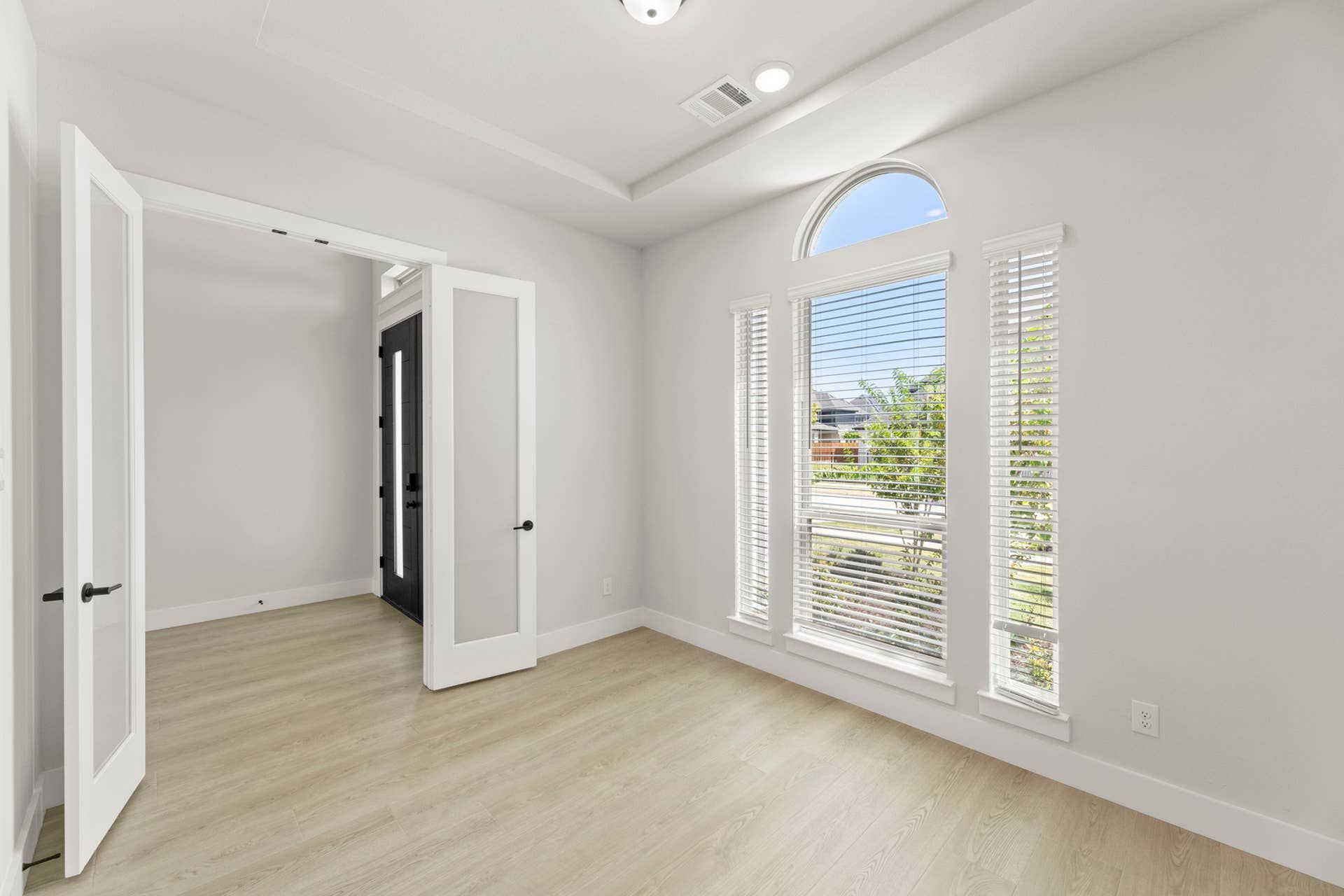 Bright study with large windows and French doors, featuring light wood flooring.