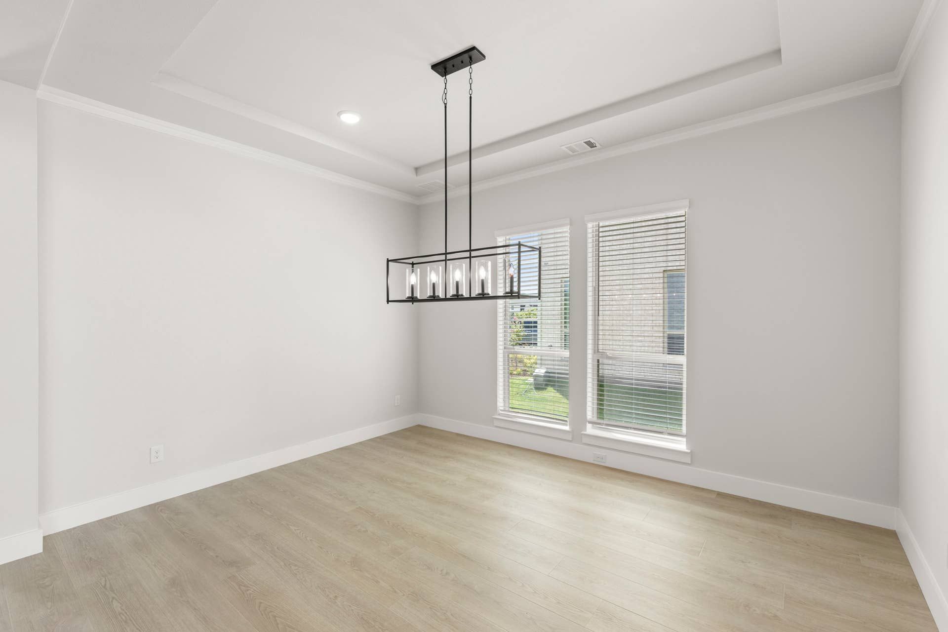 Modern dining room with tray ceiling and large windows.