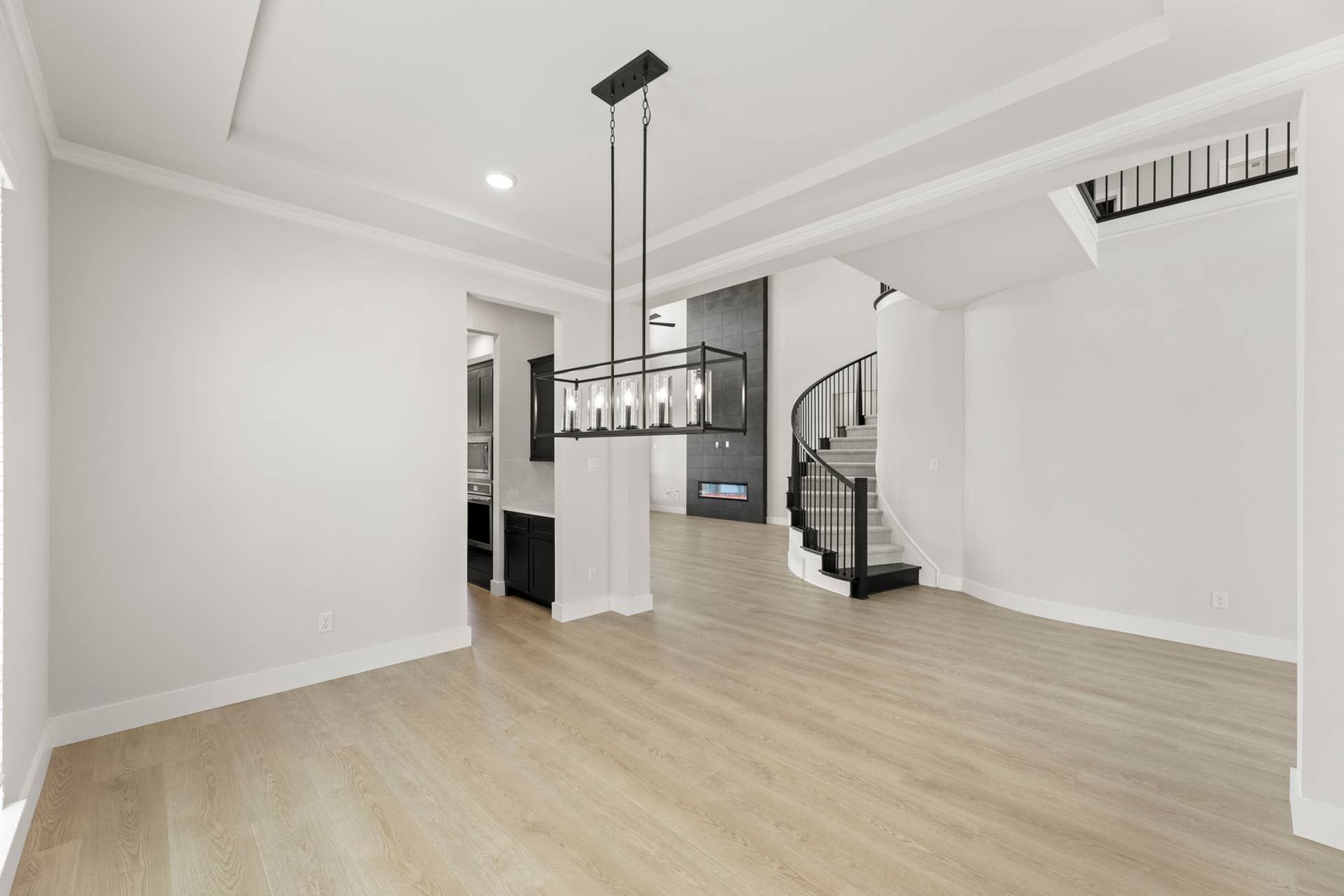 Spacious dining area with modern chandelier and curved staircase.