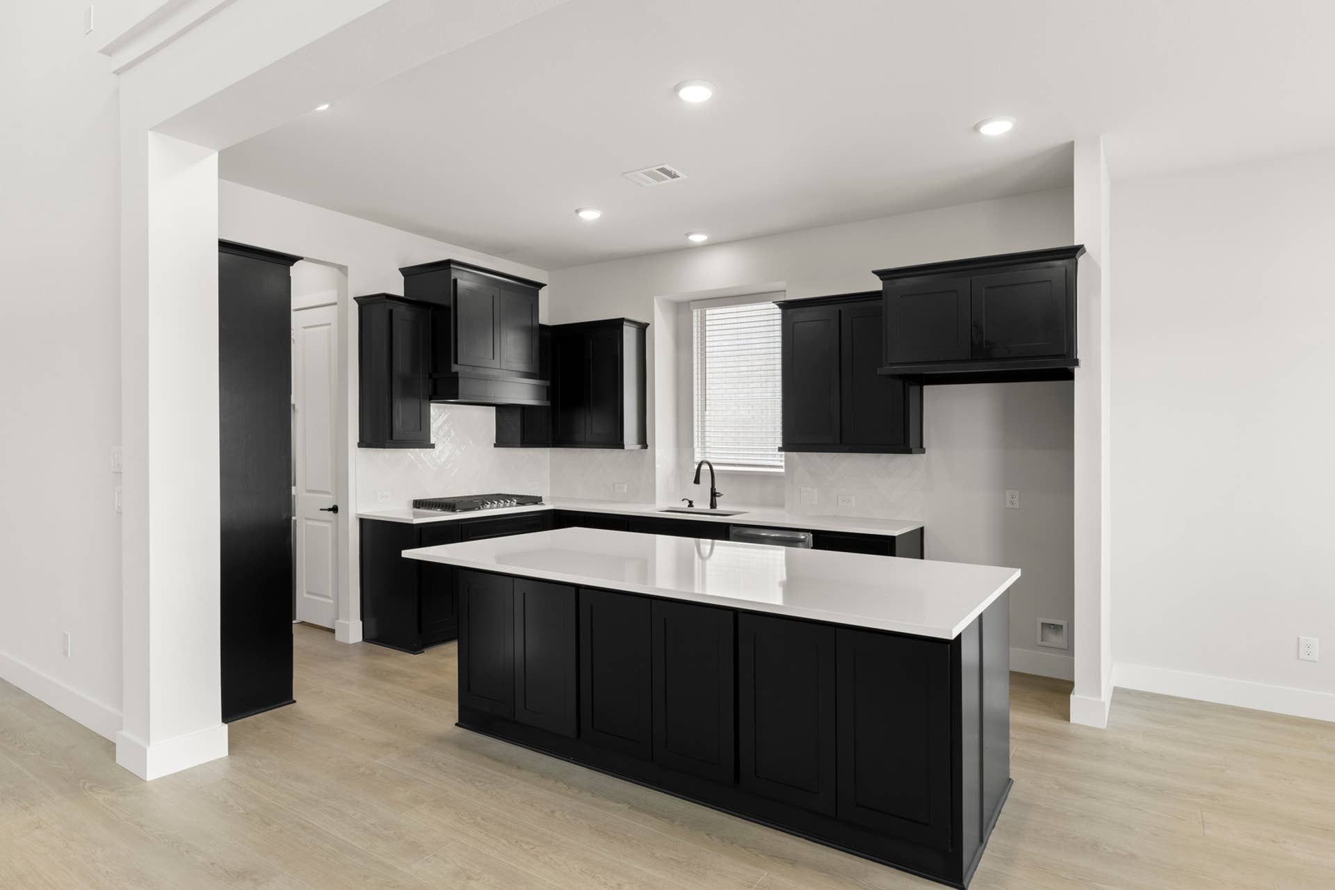 Modern kitchen with black cabinetry, white countertops, and light wood flooring.