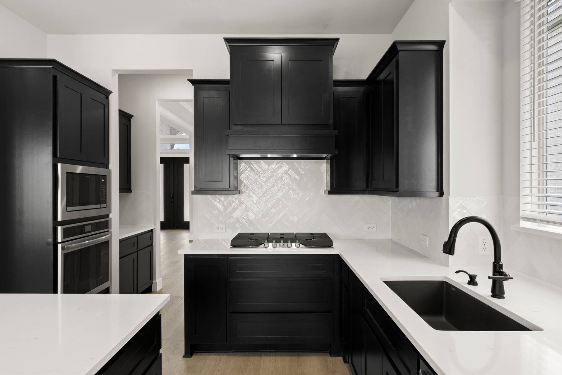 Modern kitchen with black cabinetry, white countertops, and herringbone tile backsplash.