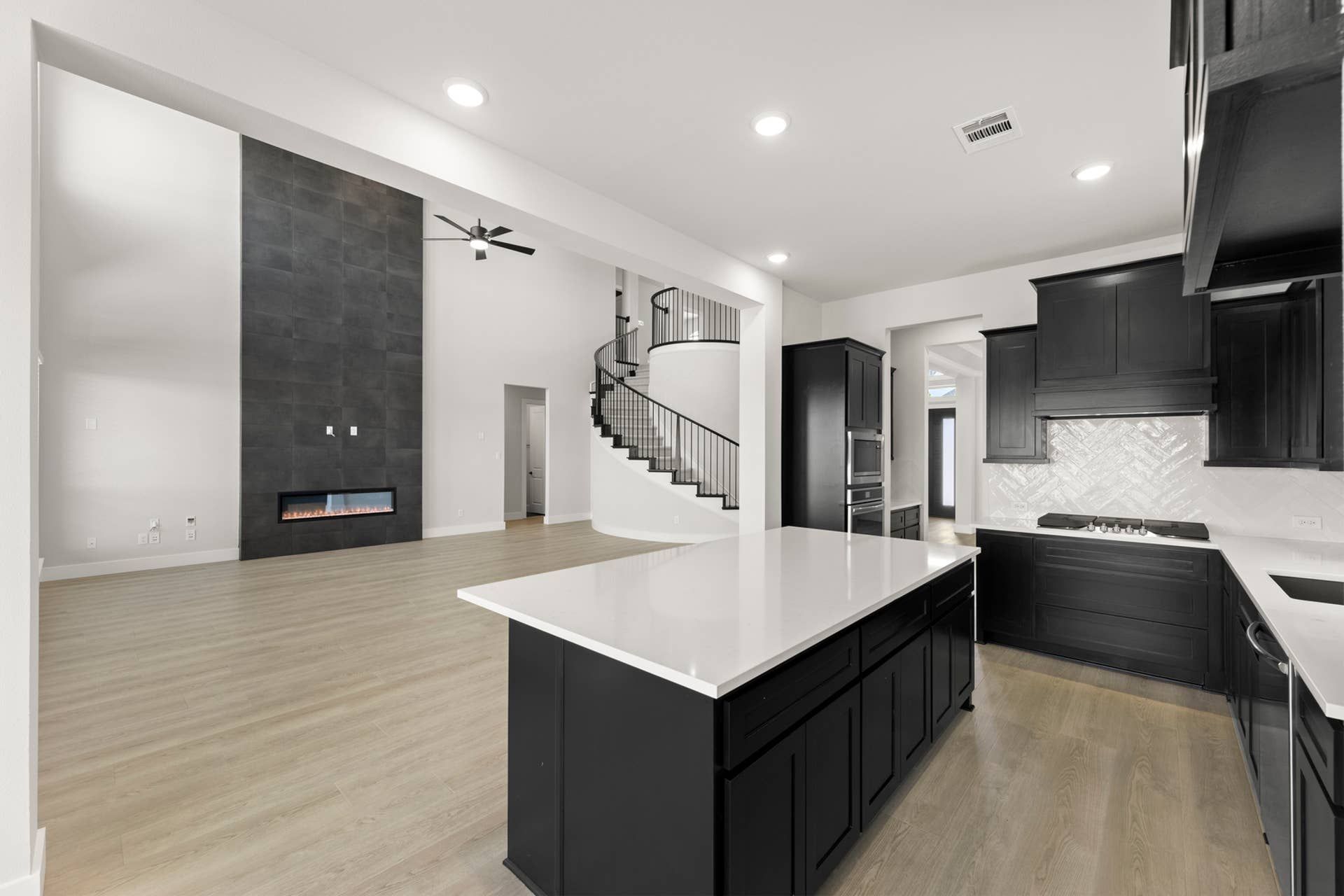 Spacious modern kitchen with black cabinetry, island, and open living area with fireplace.