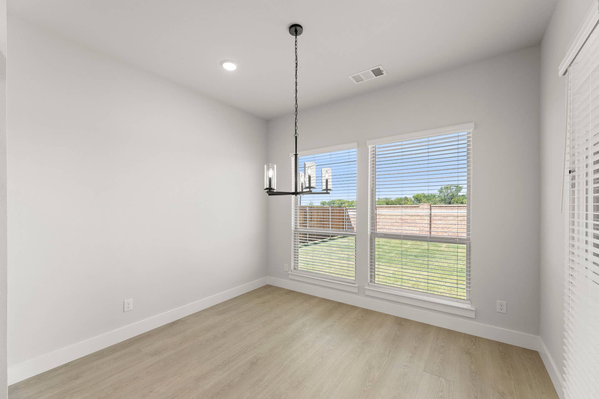 Bright dining nook with modern chandelier and large windows overlooking backyard.