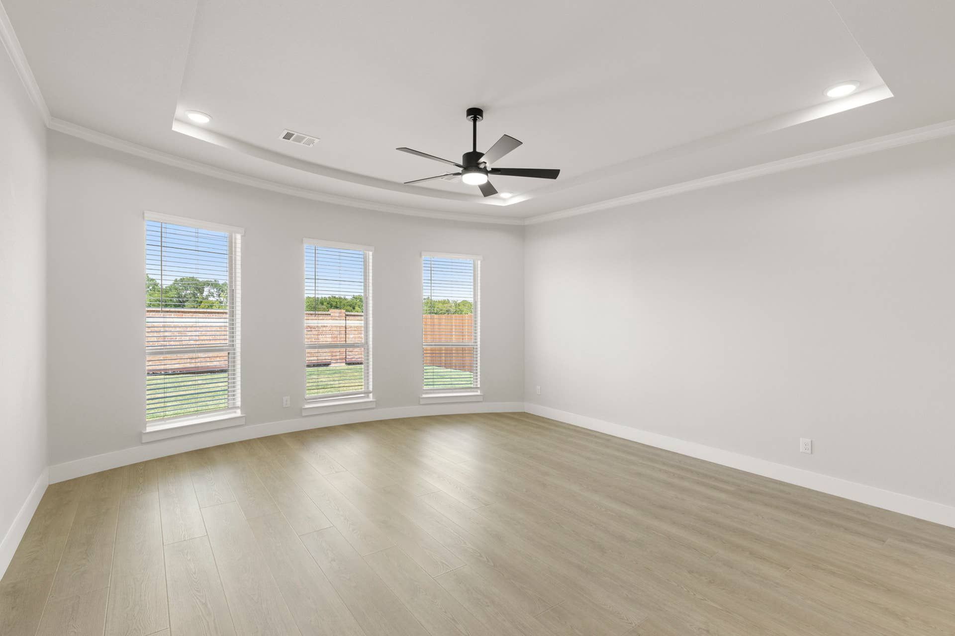 Spacious, bright room with wood flooring and large windows overlooking fenced yard.