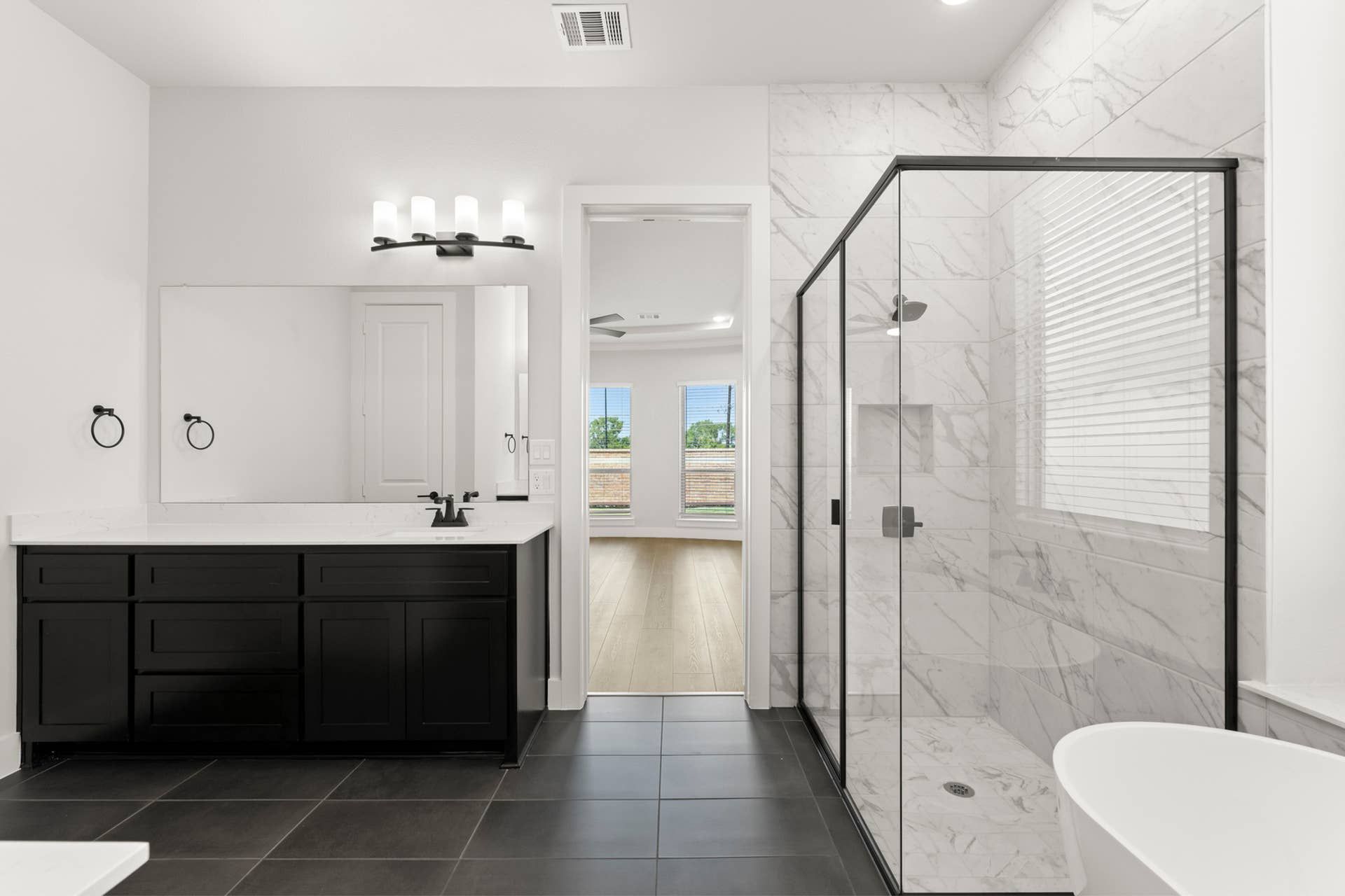 Modern bathroom with dark vanity, glass shower, and freestanding tub.