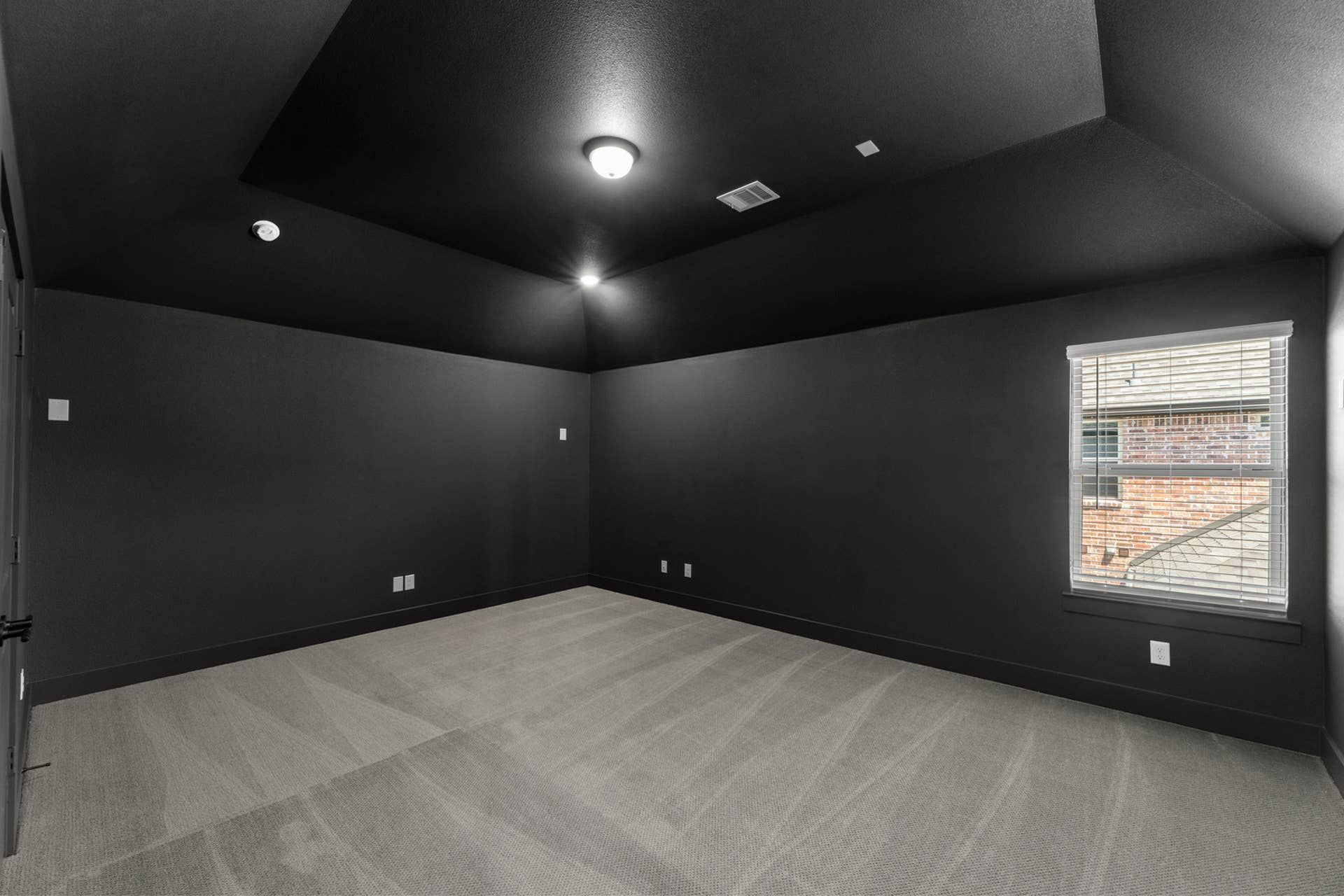 Spacious dark-themed room with carpeted floor and single window.