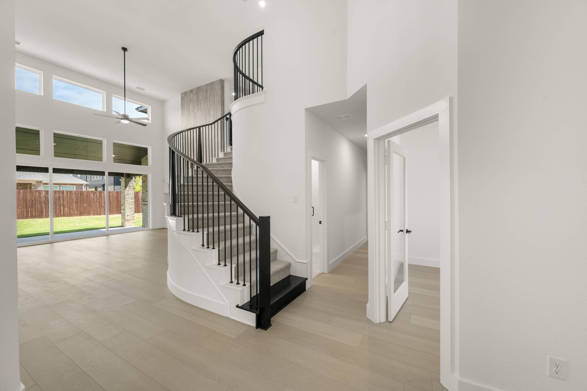 Elegant foyer with curved staircase and large windows overlooking backyard.
