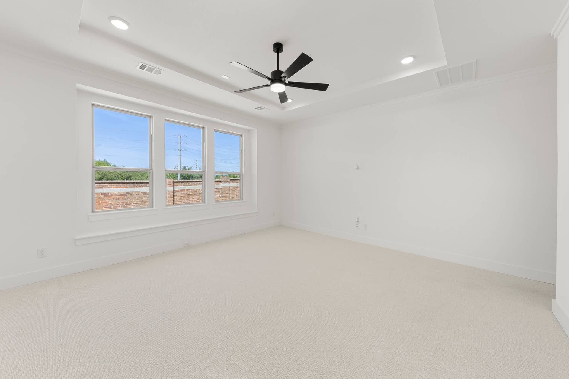 Spacious empty room with modern ceiling fan and large windows.