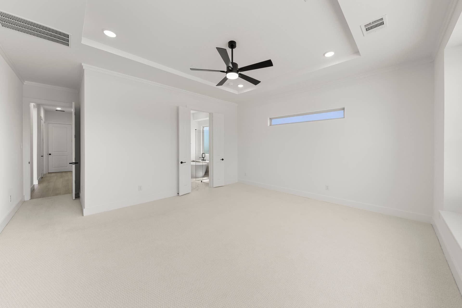 Spacious modern bedroom with tray ceiling and sleek ceiling fan.