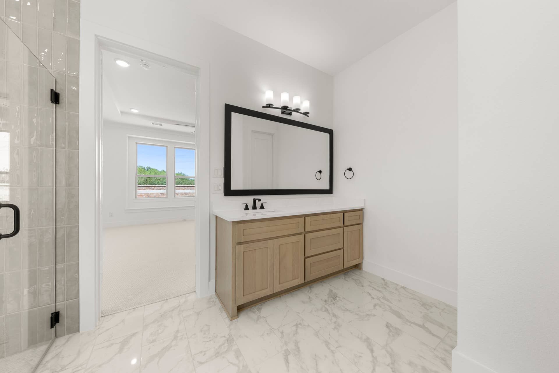 Modern bathroom with large mirror, wood vanity, and marble floor.