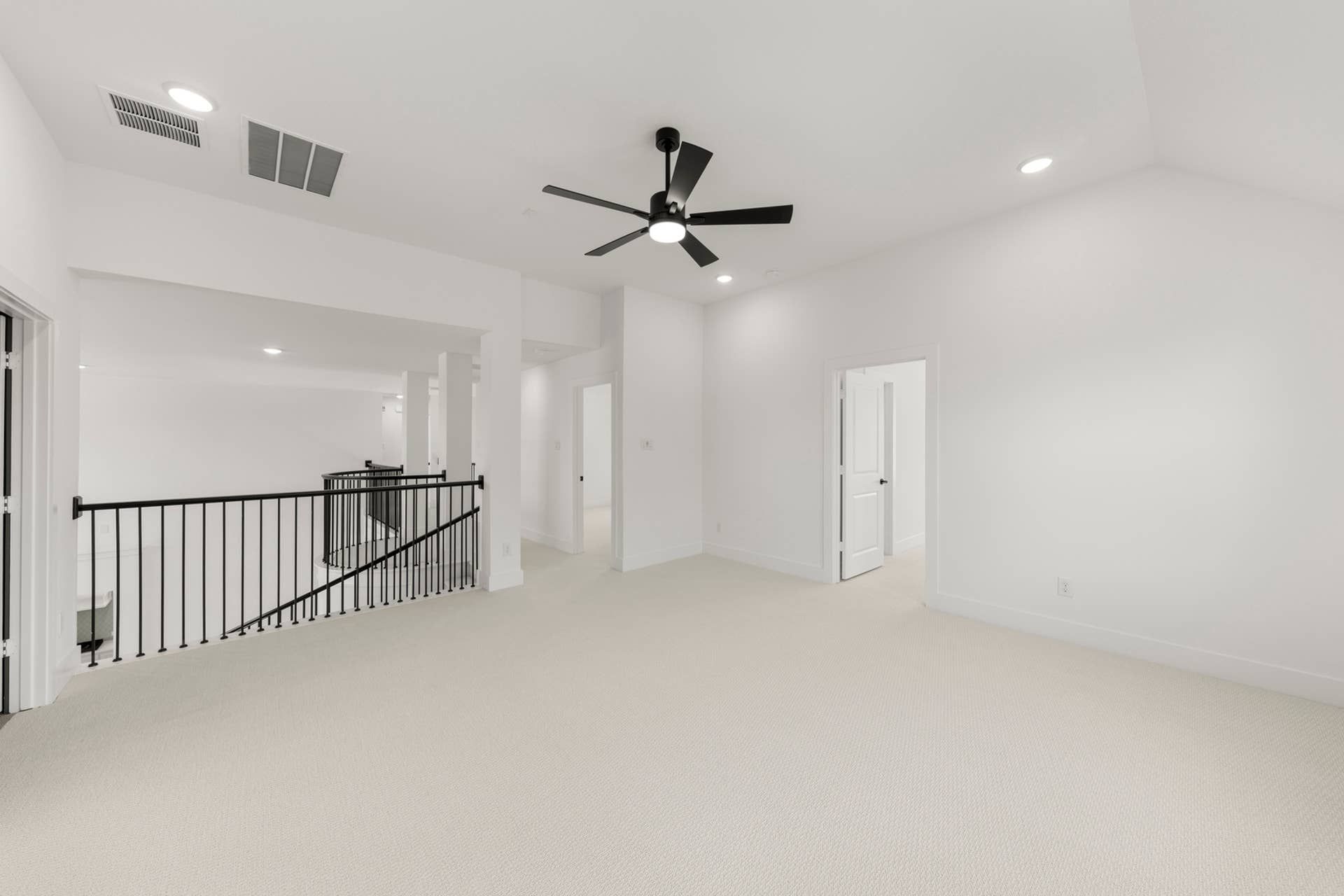 Spacious interior with ceiling fan and railing, white walls and carpeted floor.
