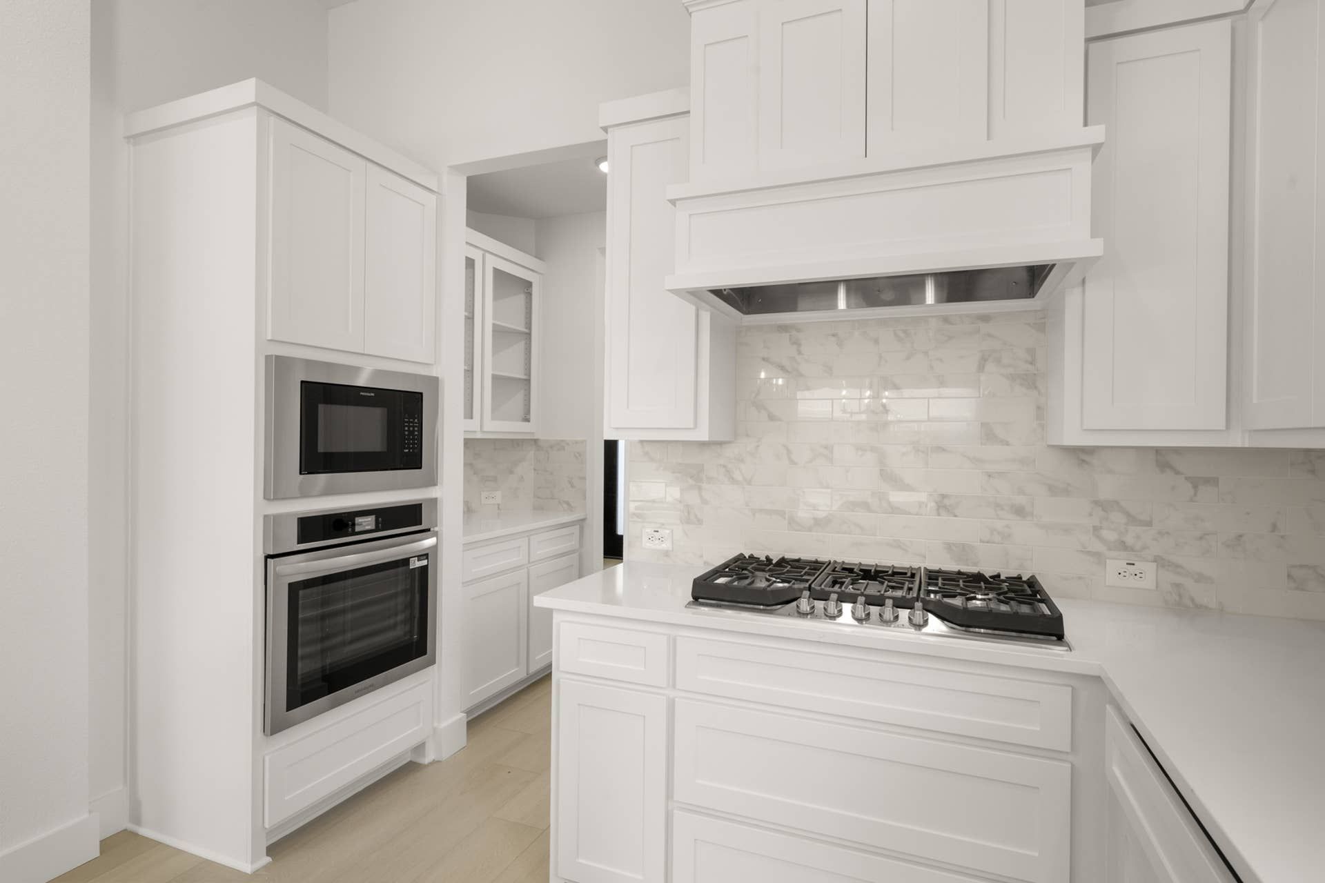 Modern kitchen with white cabinetry, marble backsplash, and stainless steel appliances.