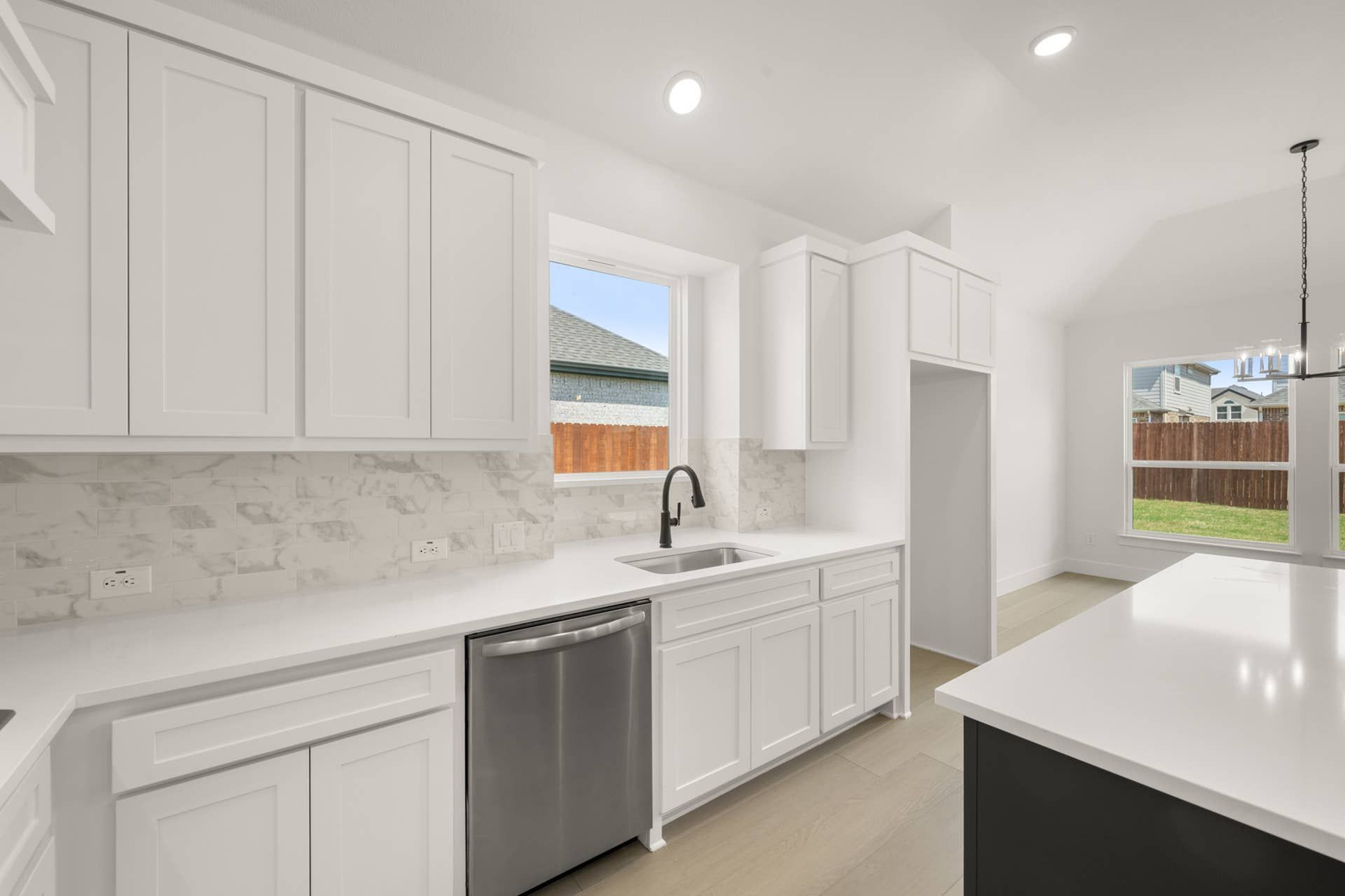 Modern kitchen with white cabinetry, marble backsplash, and stainless steel appliances.