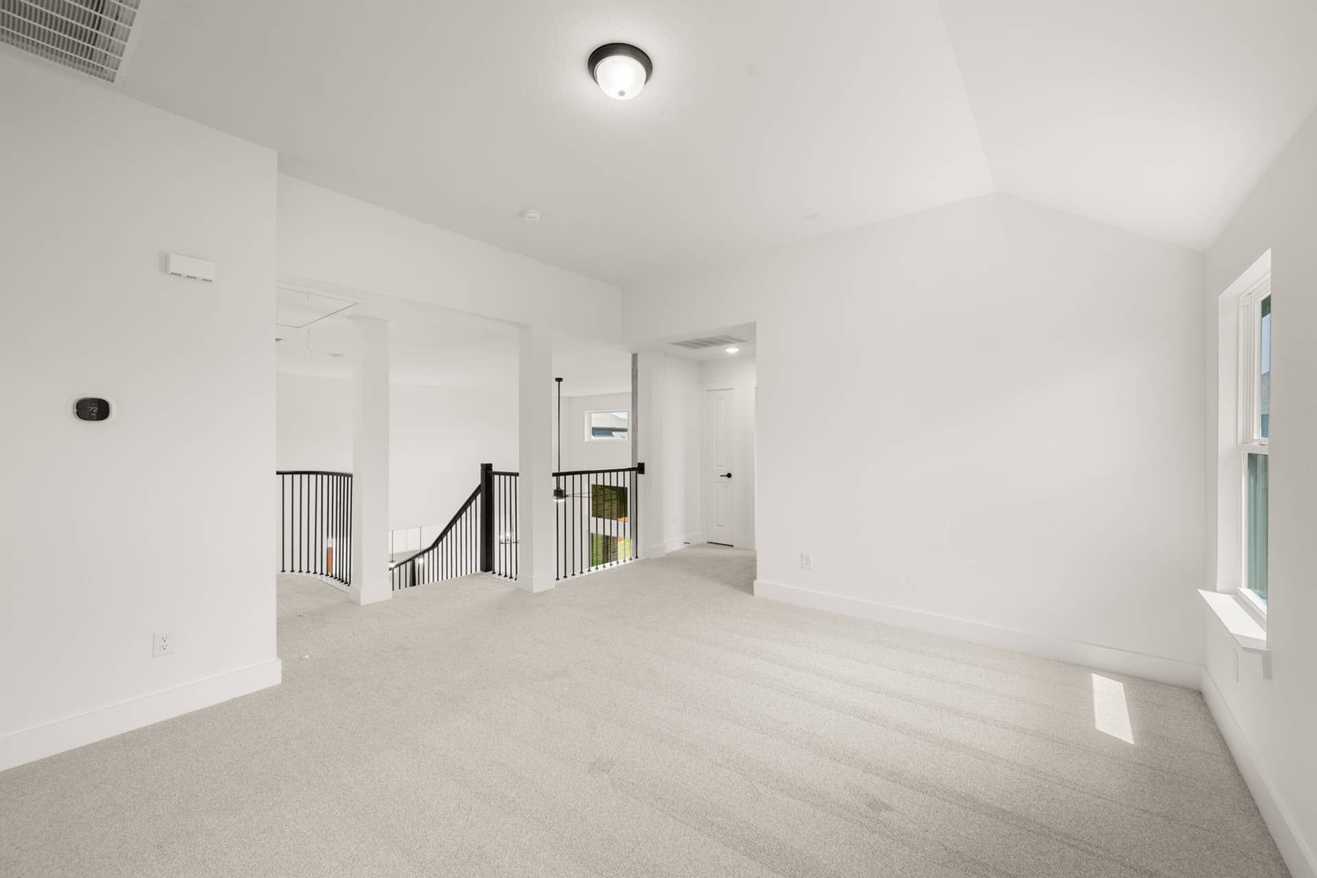 Spacious upstairs game room with carpet and natural light.
