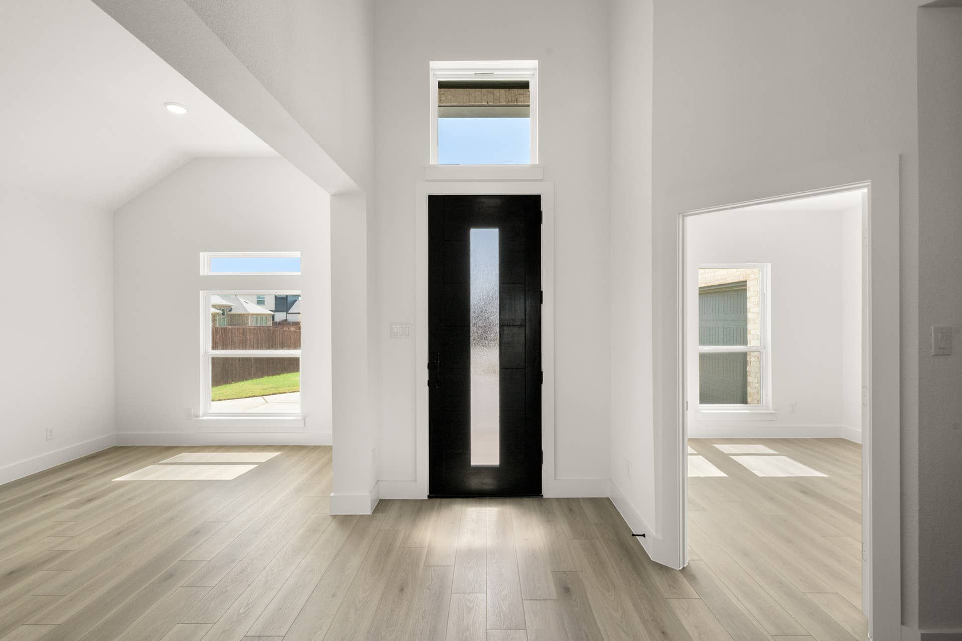 Bright entryway with modern black door and light wood flooring.