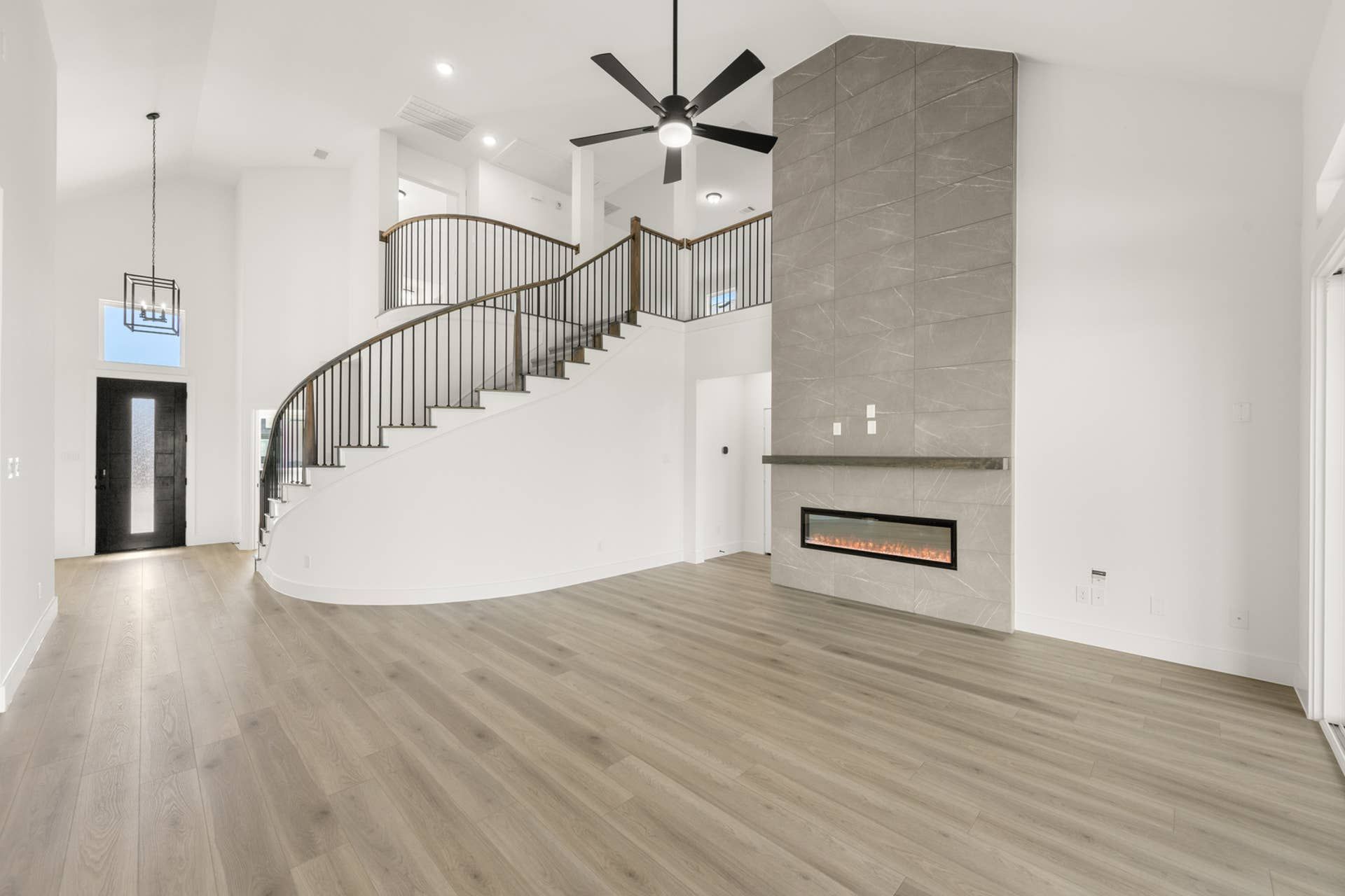 Spacious living room with curved staircase, modern fireplace, and high ceilings.