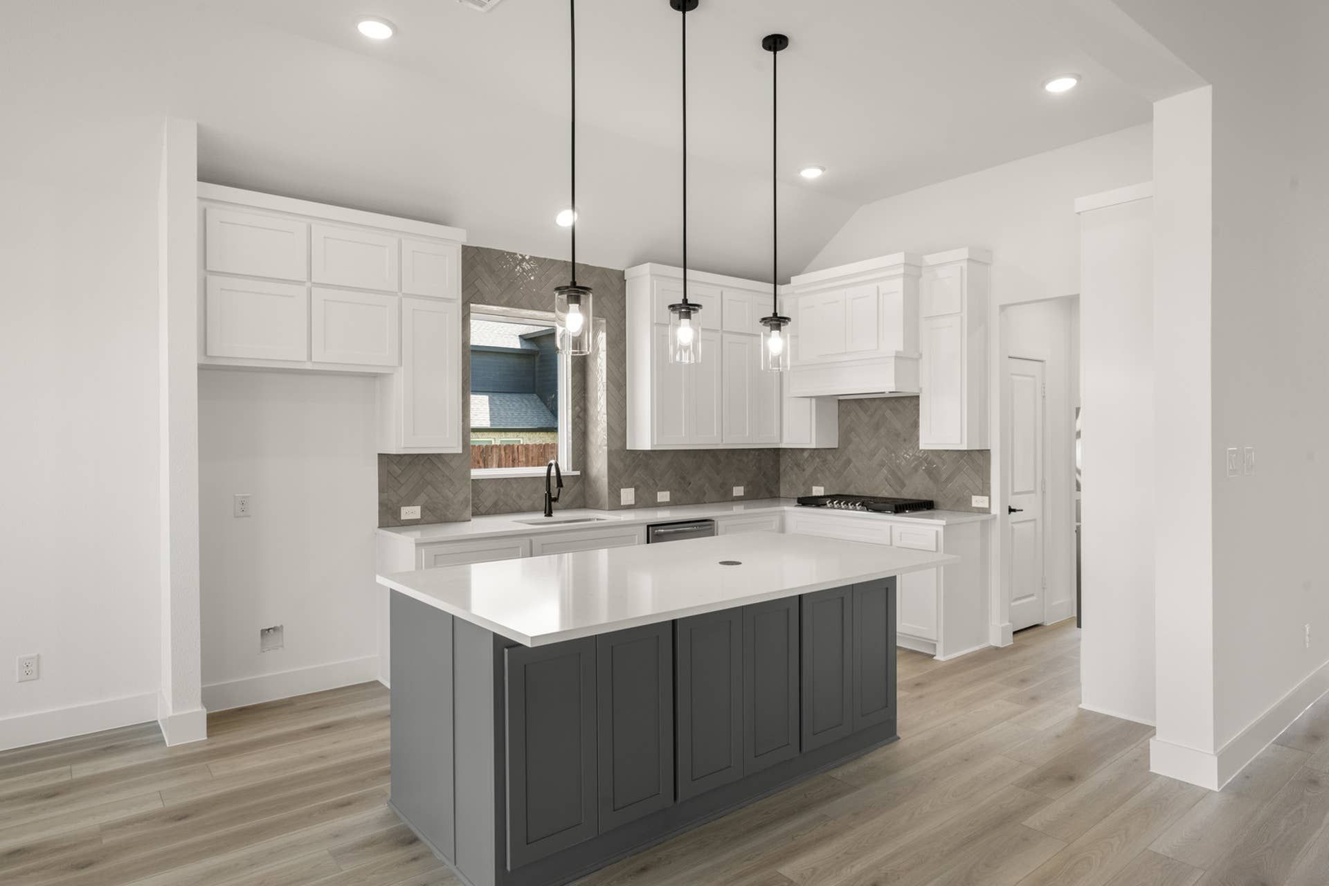 Modern kitchen with white cabinetry, island, pendant lights, and herringbone backsplash.