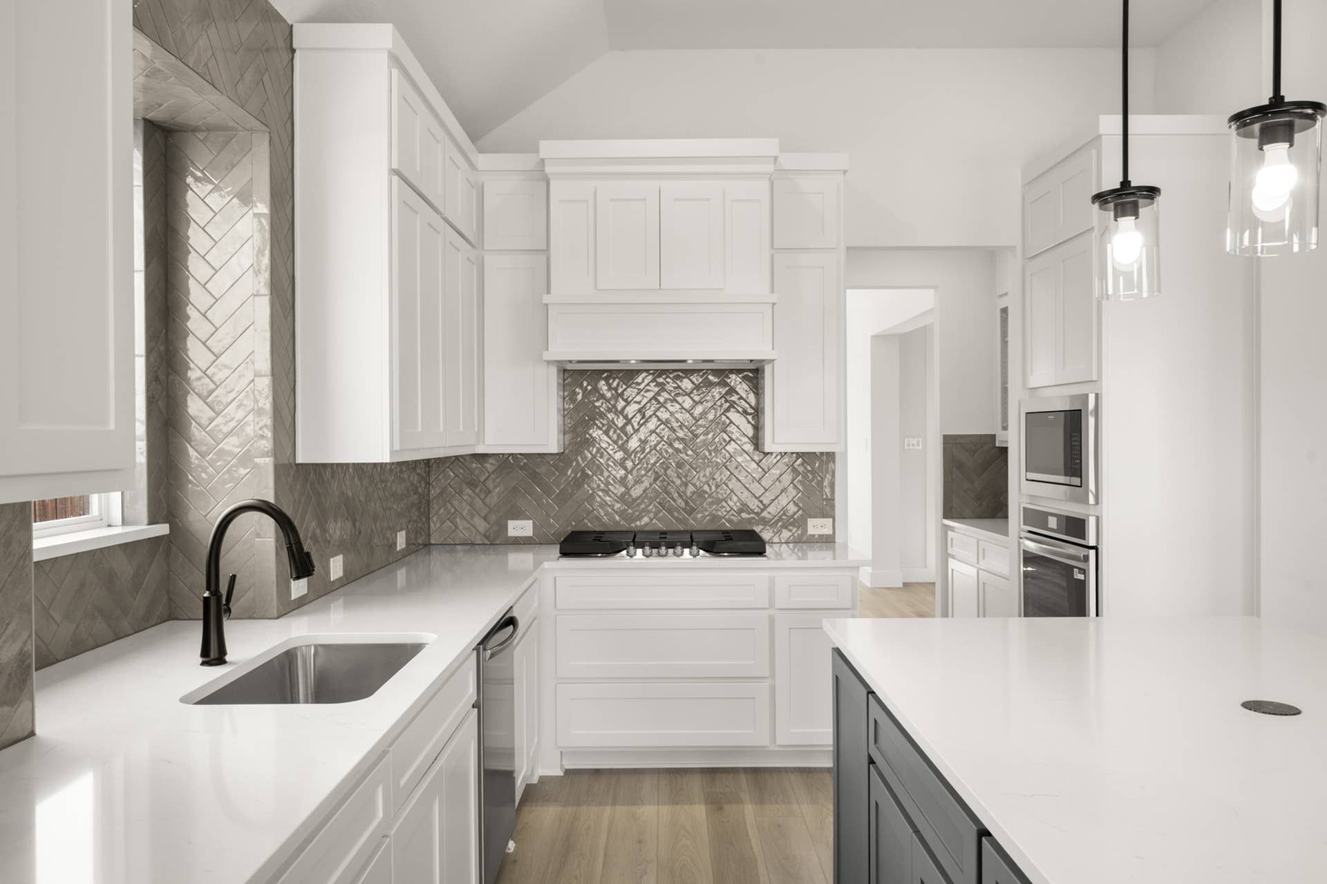 Modern kitchen with white cabinetry, herringbone backsplash, and pendant lighting.
