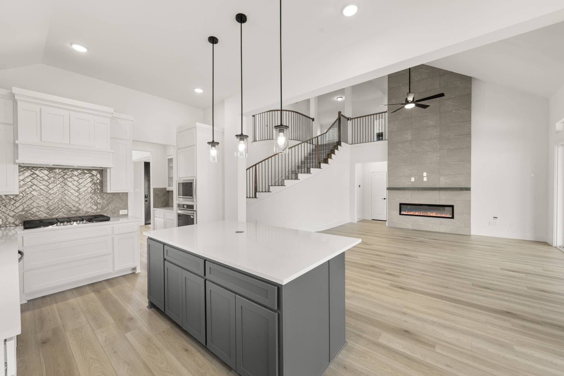 Modern kitchen with white cabinetry, island, pendant lights, and open living space.