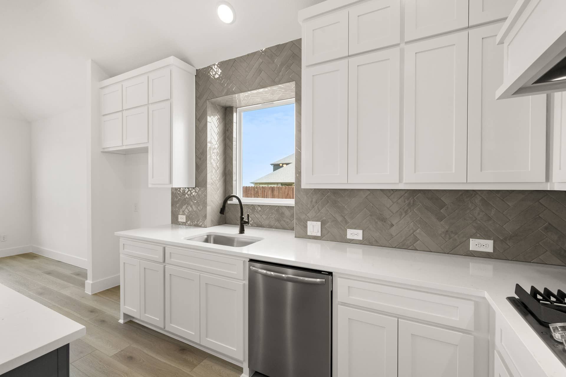Modern kitchen with white cabinetry, herringbone tile backsplash, and stainless steel appliances.