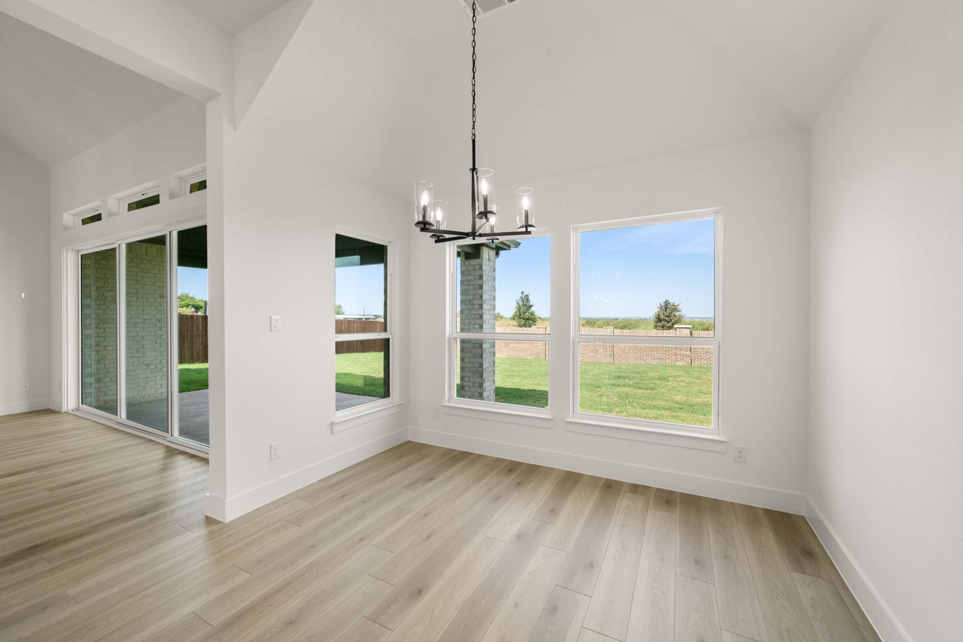 Bright dining area with large windows and modern chandelier overlooking backyard.