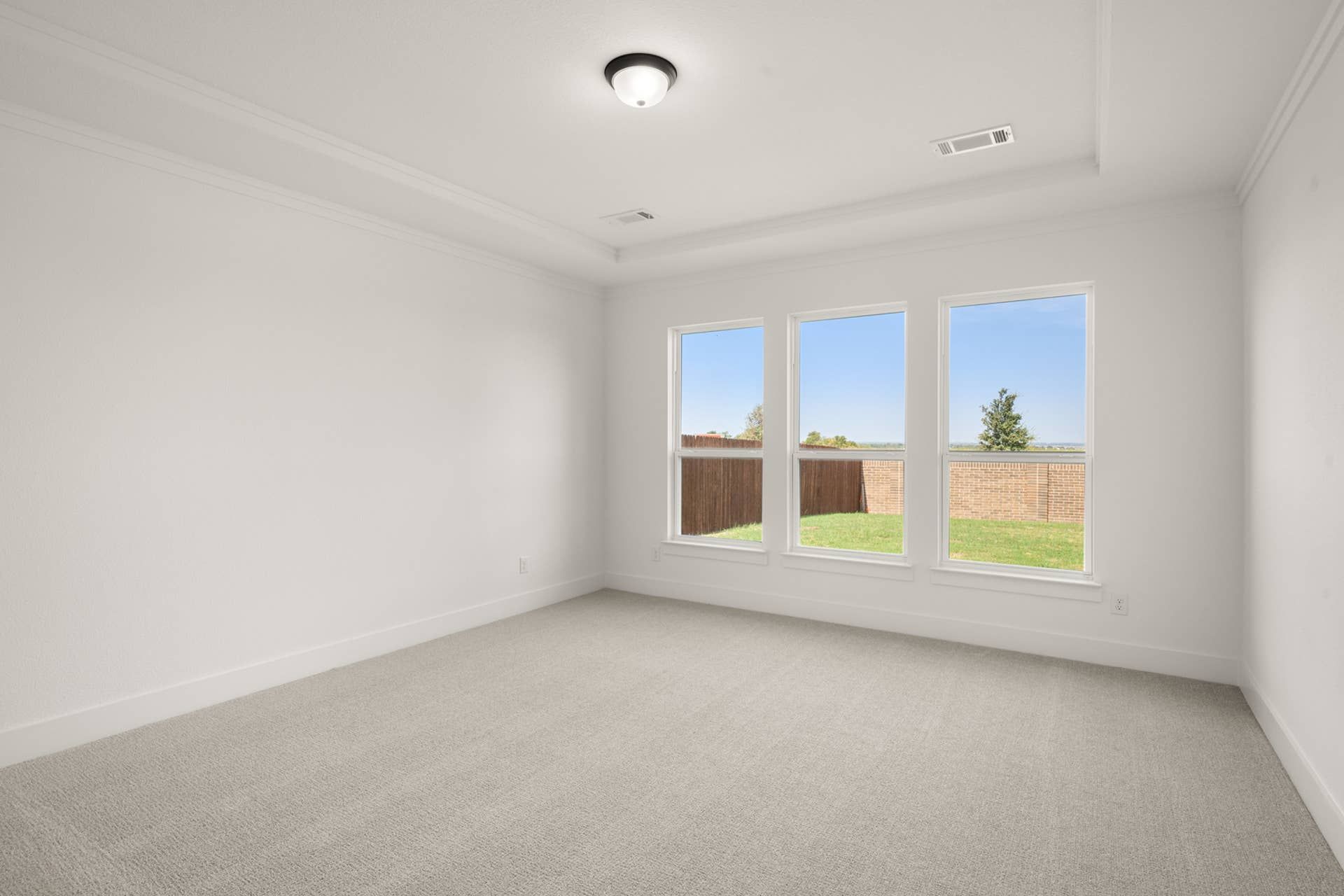 Spacious primary suite with carpet flooring and large windows overlooking a fenced yard.