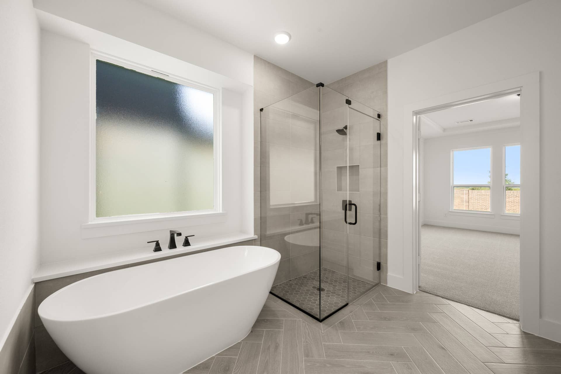 Modern bathroom with freestanding tub, glass shower, and frosted window.