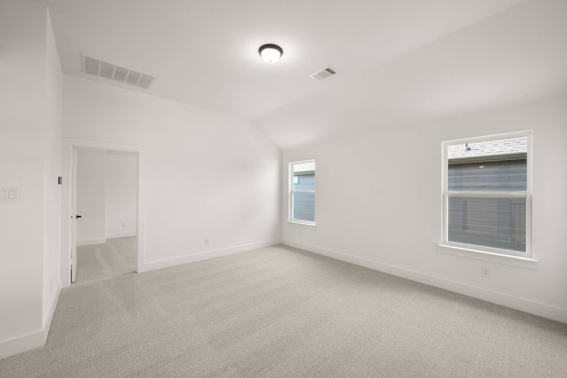 Spacious empty game room with plush carpet and natural light from two windows.