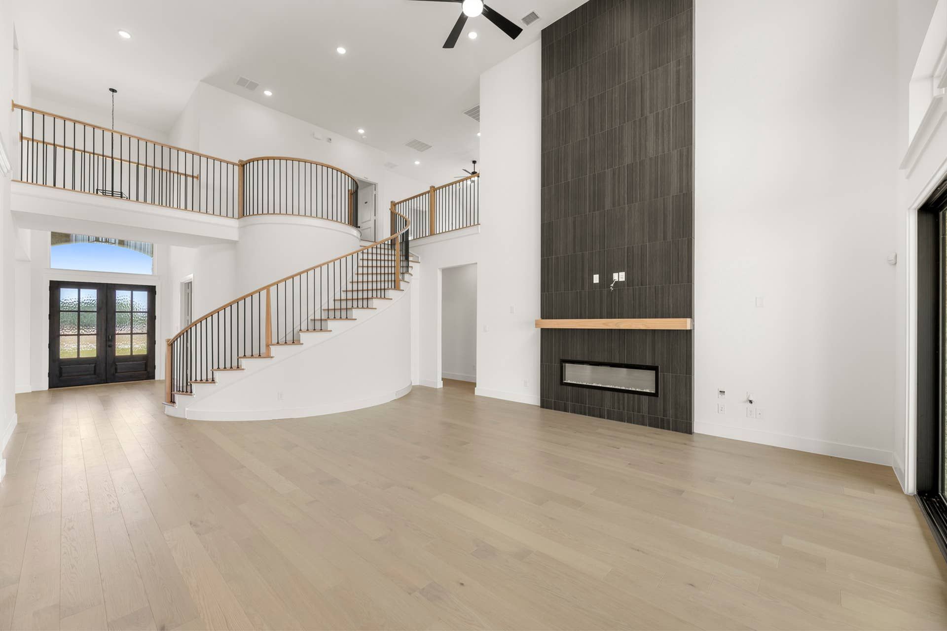 Spacious interior with curved staircase, high ceilings, and modern fireplace.