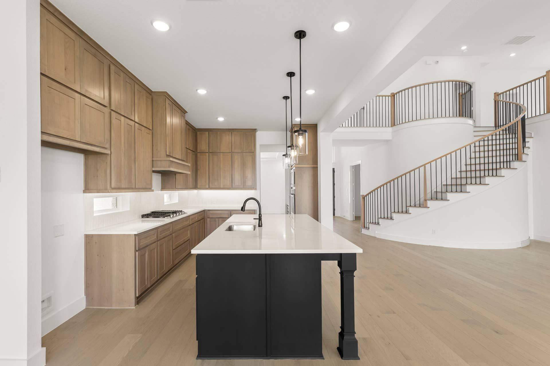 Modern kitchen with island, wooden cabinetry, and spiral staircase in open-concept home.