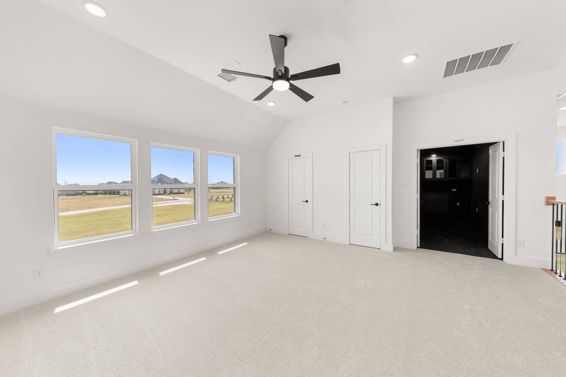 Spacious interior room with large windows, ceiling fan, and neutral carpeting.