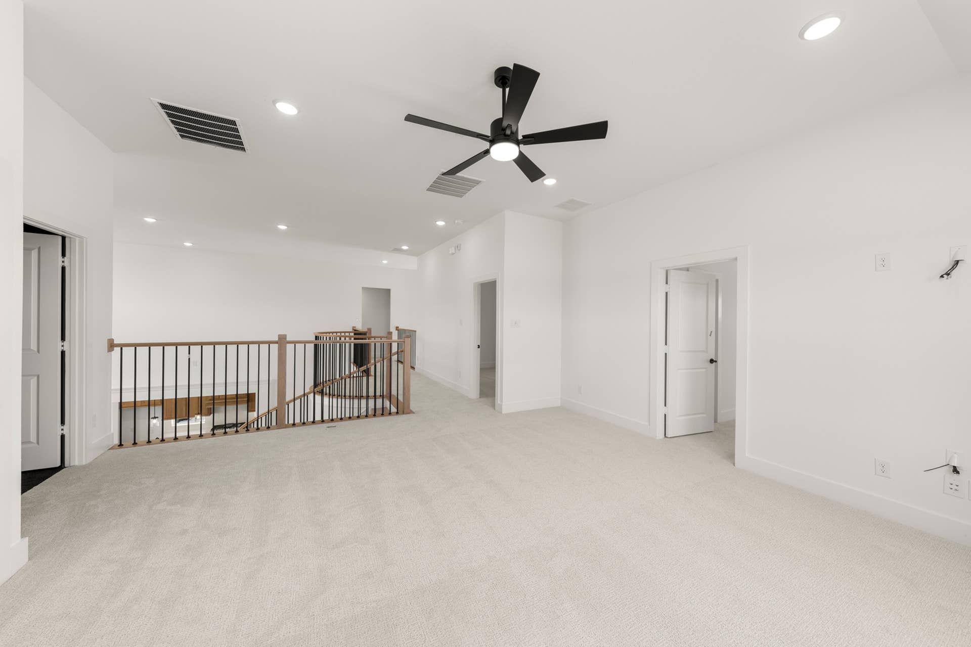 Spacious interior with ceiling fan, carpeted floor, and wooden railing.