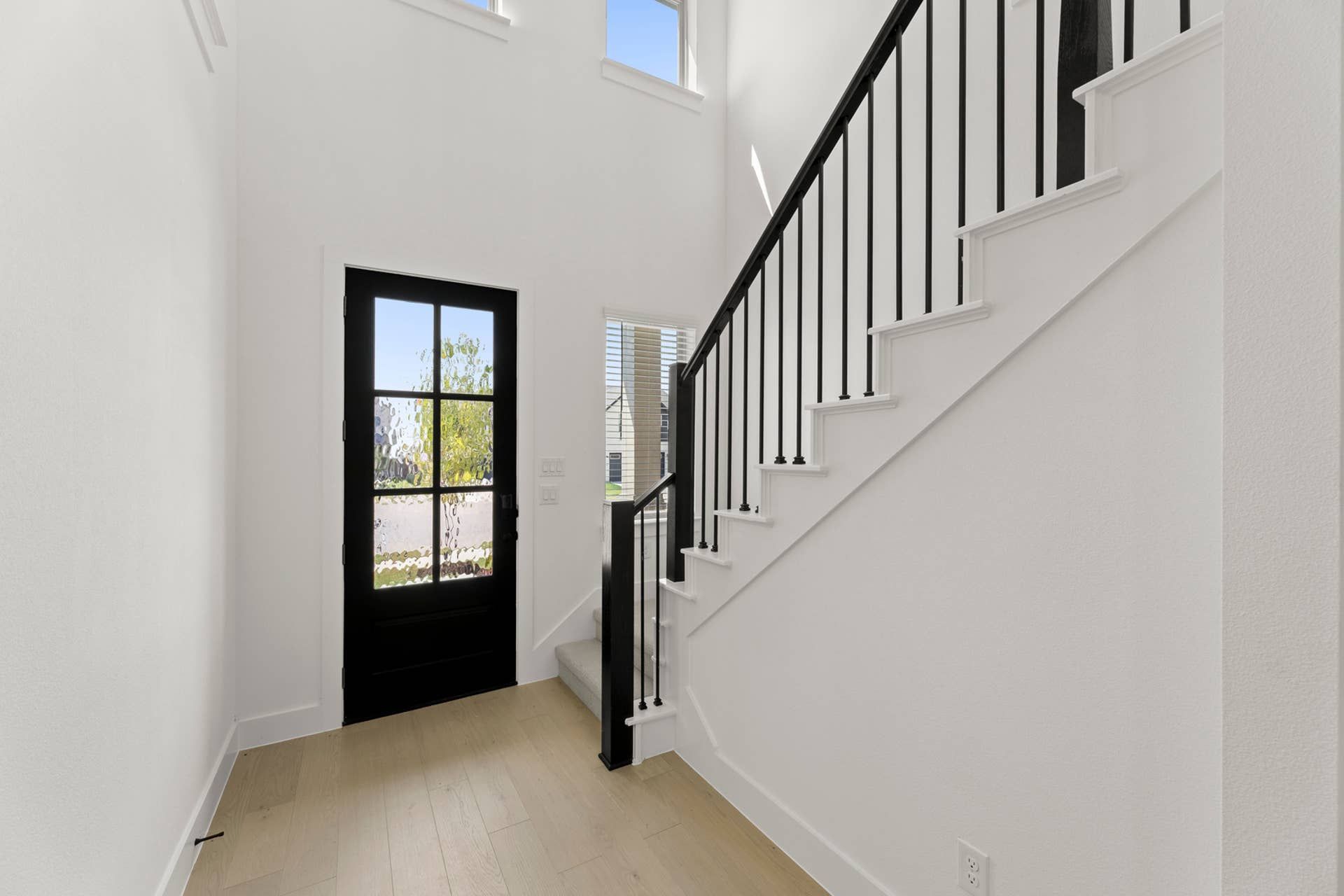 Modern entryway with black door and staircase in bright interior.