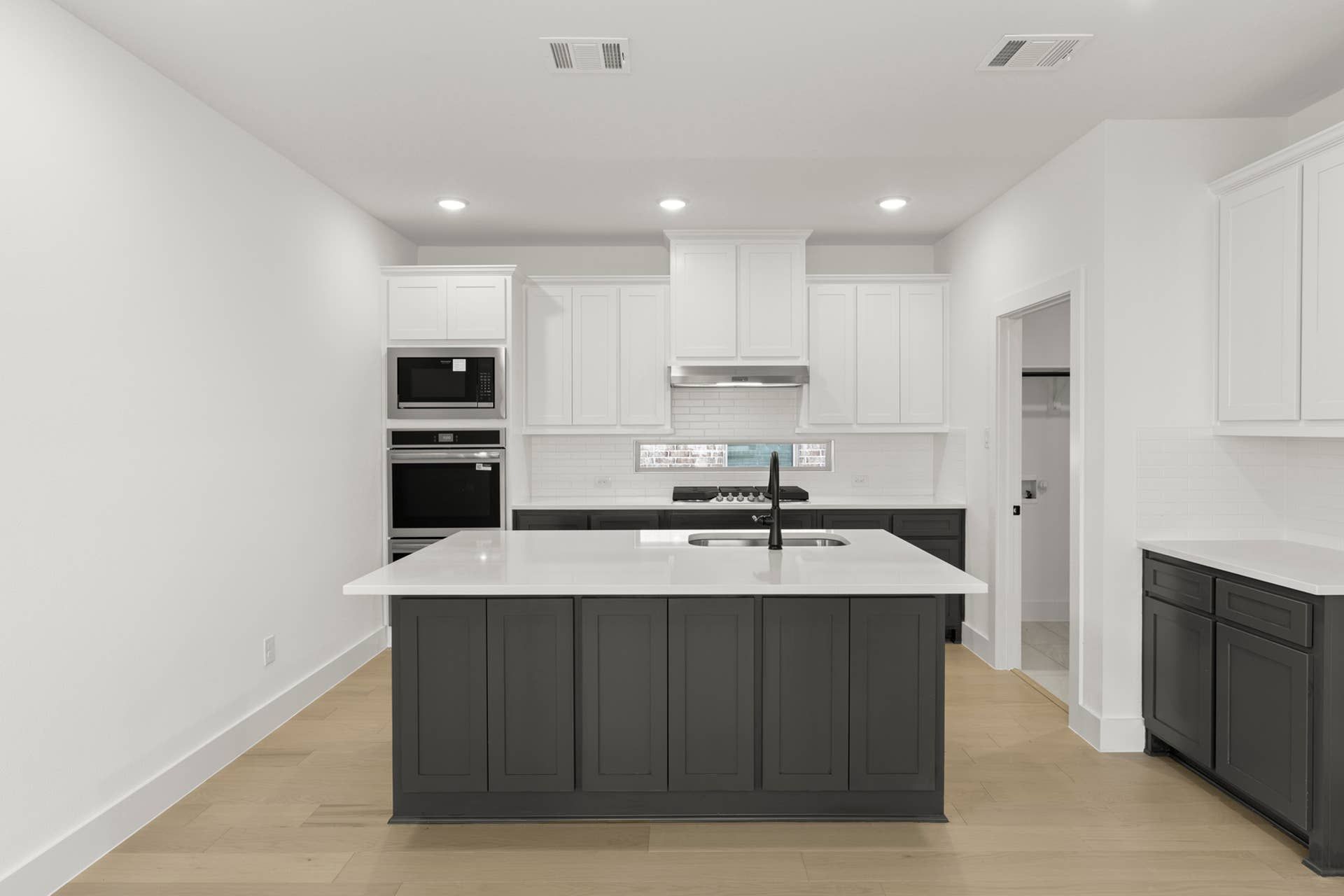 Modern kitchen interior with large island, white cabinetry, and stainless steel appliances.