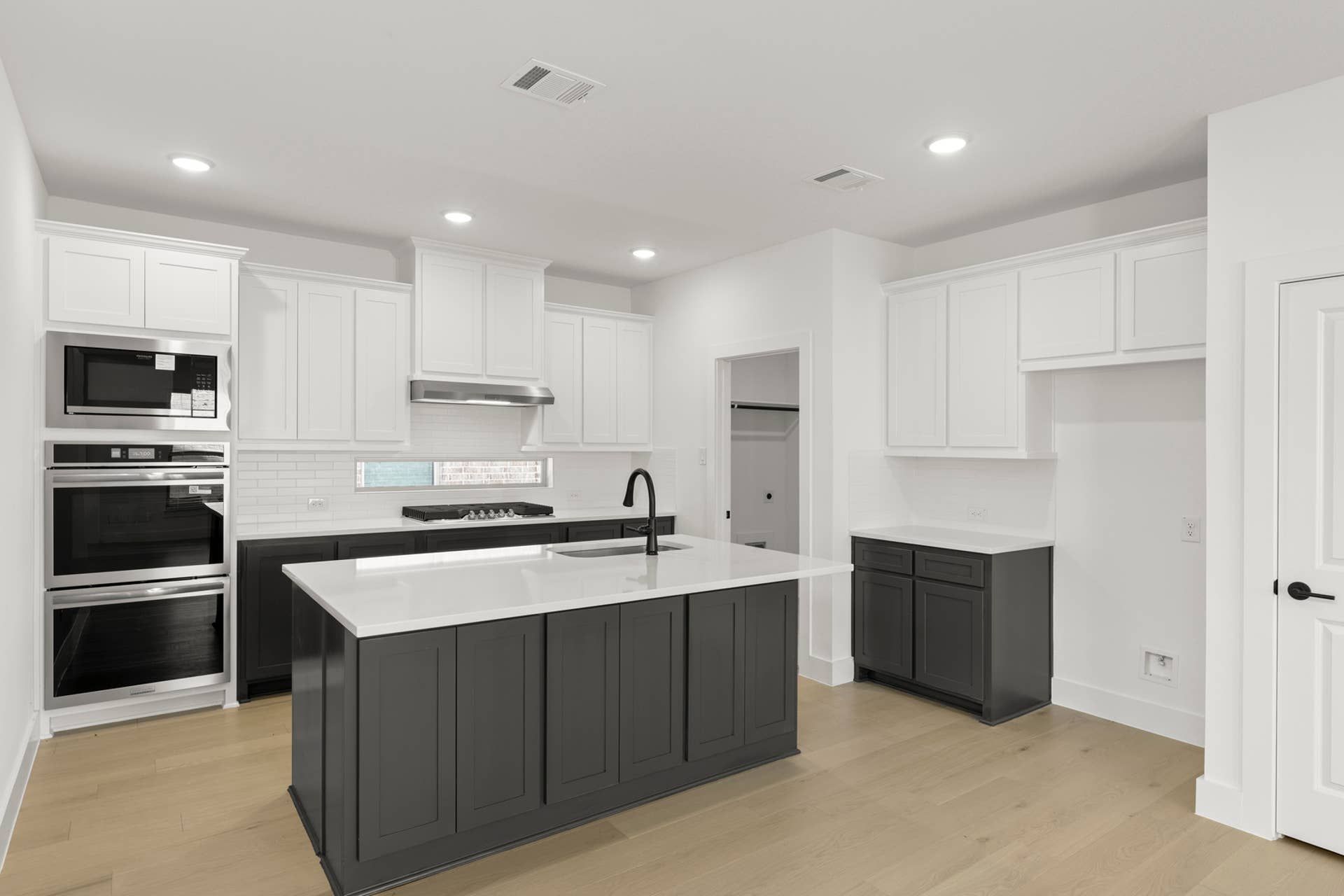 Modern kitchen with white cabinets, dark island, and stainless steel appliances.