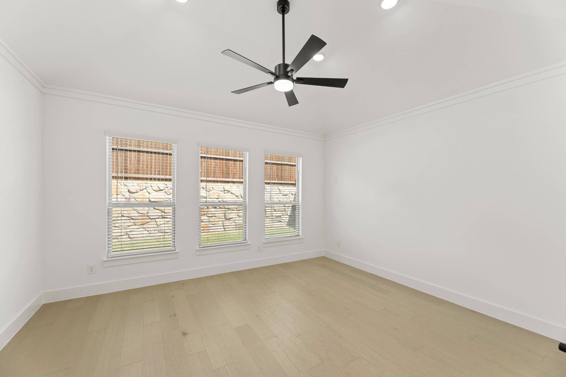 Bright room with ceiling fan and three large windows, light wood flooring.