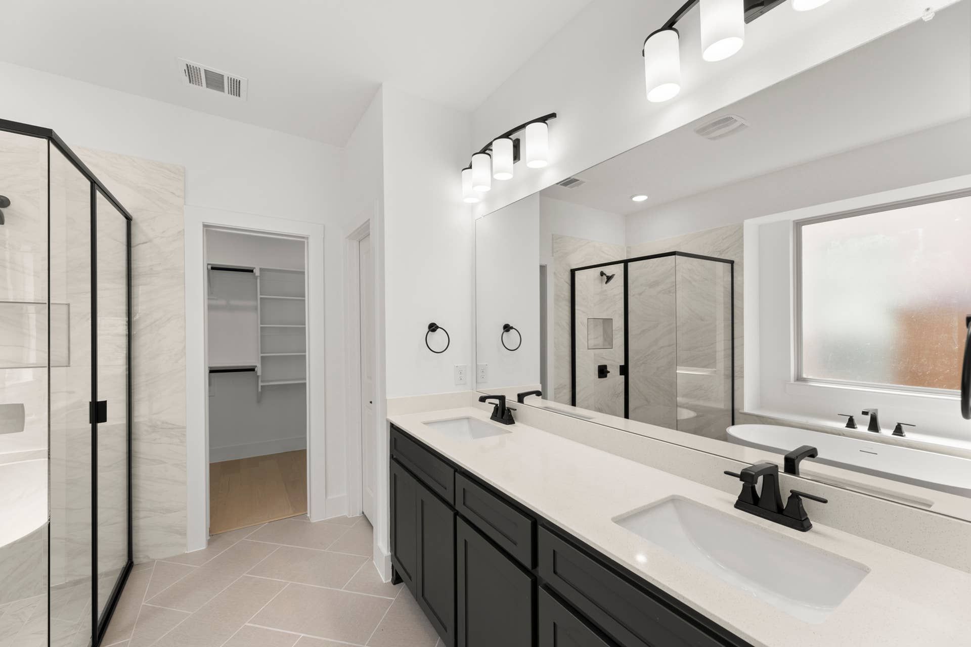 Modern bathroom with dual sinks, glass shower, and walk-in closet.